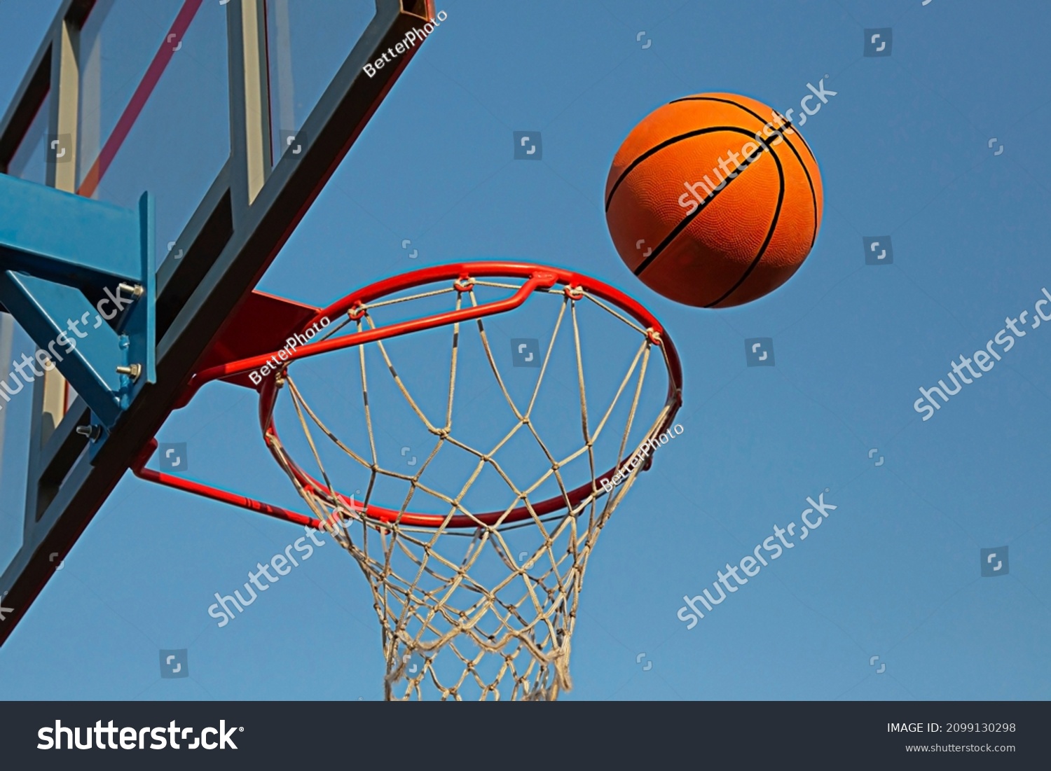 A basketball in a net on a blue sky background. The ball hit the ring. Sports, team game. Conceptual: victory, success, hitting the target, sport.  #2099130298