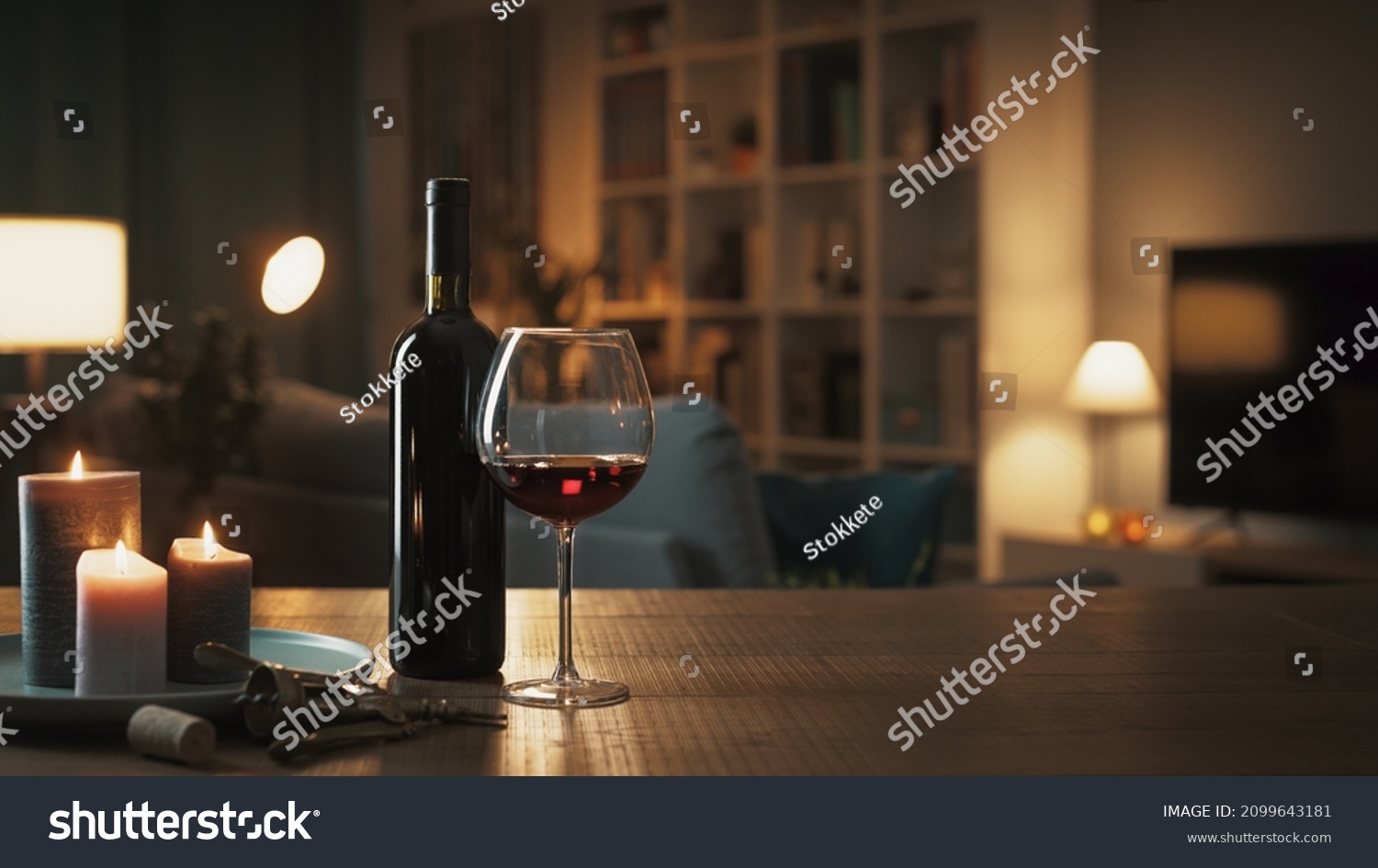 Red wine tasting at home: wine bottle, wineglass, corkscrew and candles on a table in the living room at night #2099643181