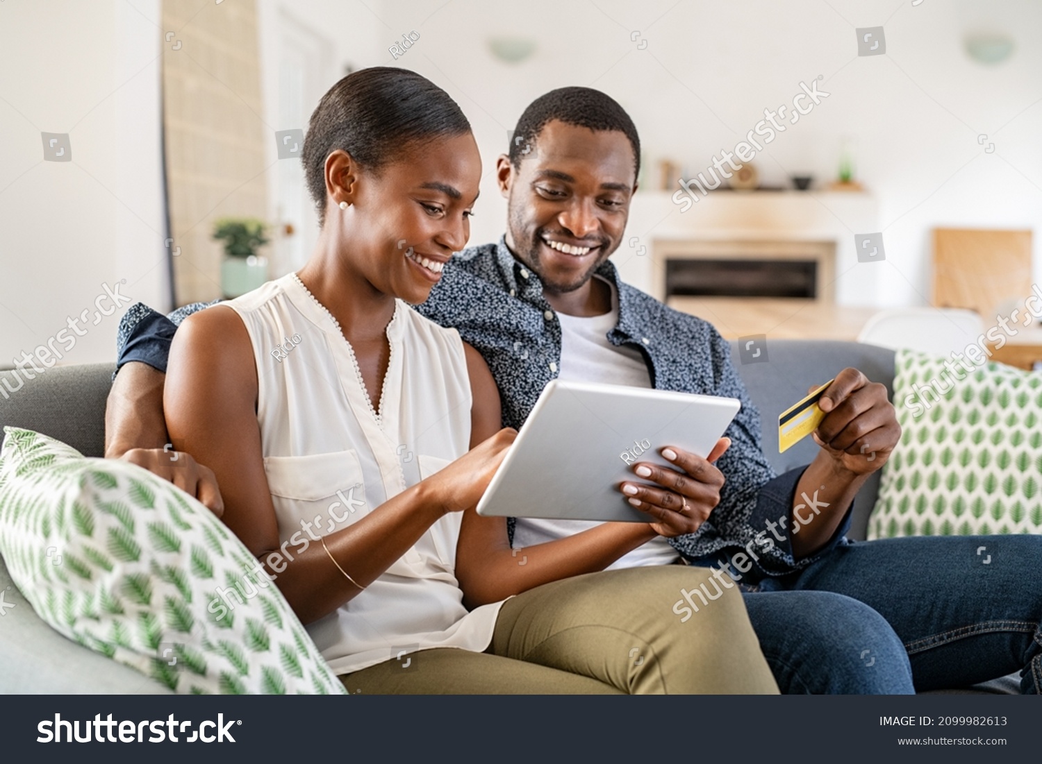 Black wife doing shopping online while using digital tablet at home with husband. Couple using bank card to pay bills or to book their next vacation. Mature couple making an online purchase. #2099982613