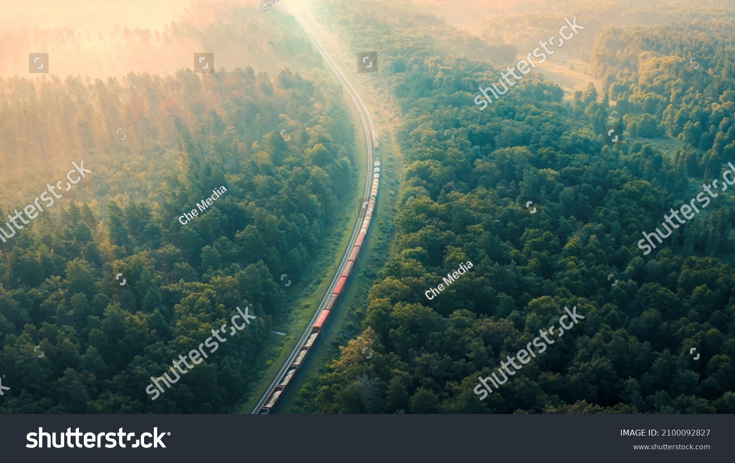 Cargo Train in summer morning forest at fog sunrise. Aerial view of moving freight train in forest. Morning mist landscape with train, railroad, foggy trees. Top aerial drone view near railway. #2100092827