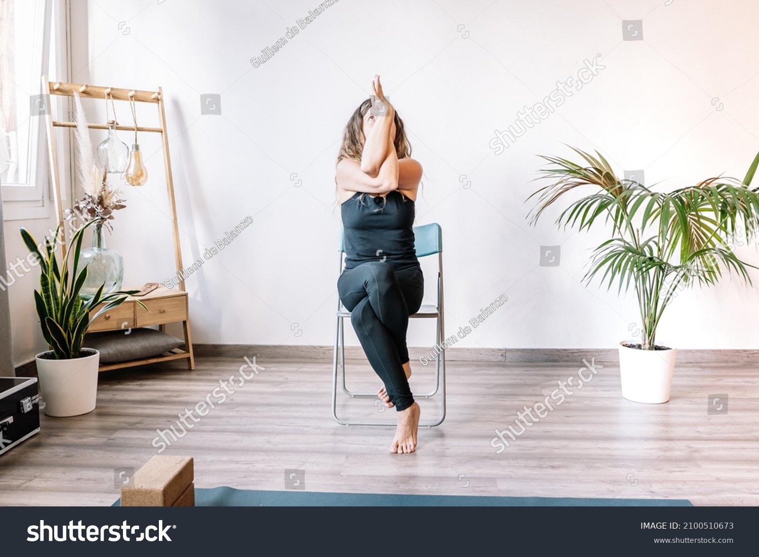 Woman doing Eagle pose on chair #2100510673