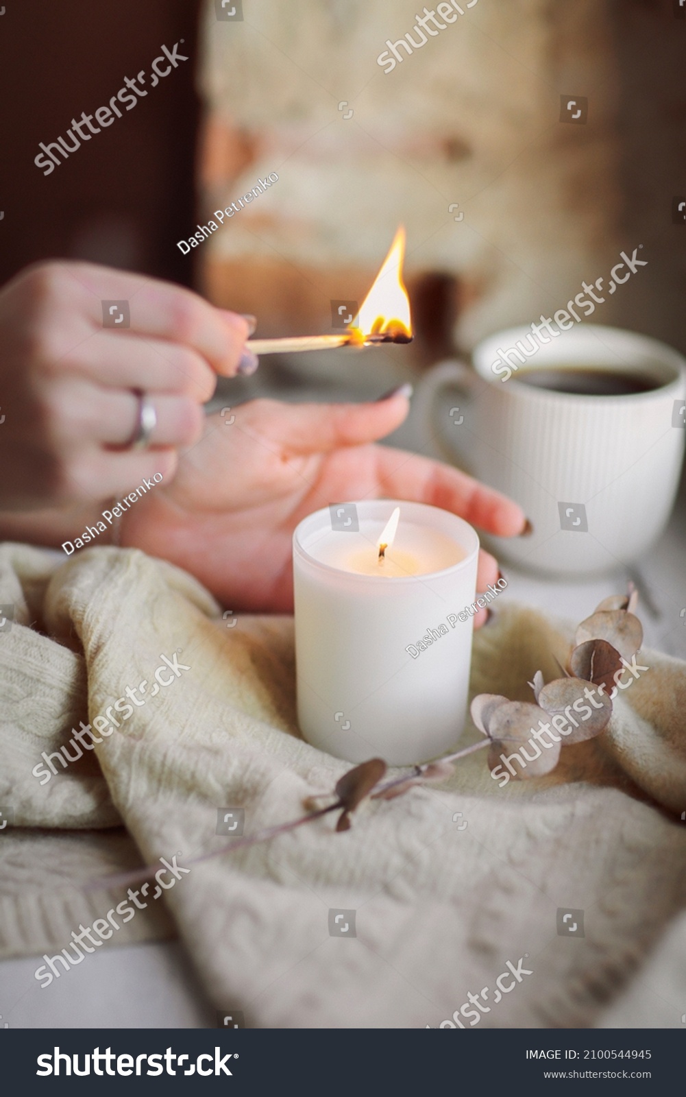 Female hands with lit match lighting burning candle on windowsill for calm and coziness at home, woman trying to create cozy warm and intimate atmosphere in cold season. Hygge lifestyle concept #2100544945