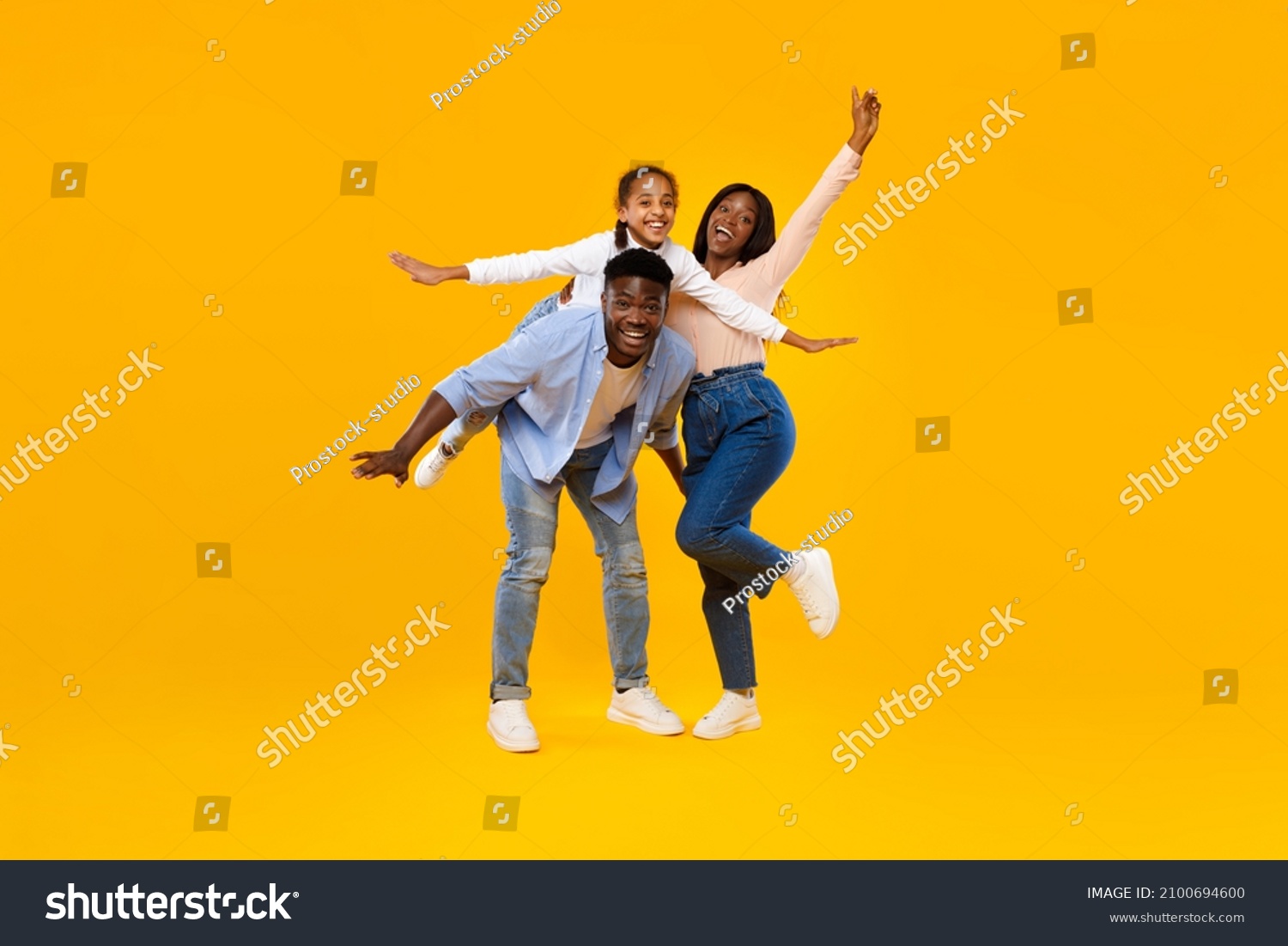 Spending Time With Family Is Fun. Full body length of excited African American man, woman and girl laughing and posing isolated on yellow studio wall. Cheerful father carrying daughter on back, banner #2100694600