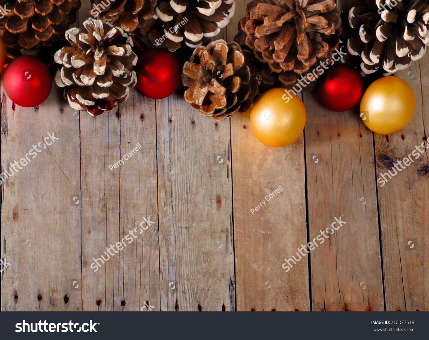 Christmas background of pine cones and Christmas balls on a rustic wooden surface. The decorations are gold and red. Some of the pine cones have fake snow tipped scales. Plenty of copy space #210077518