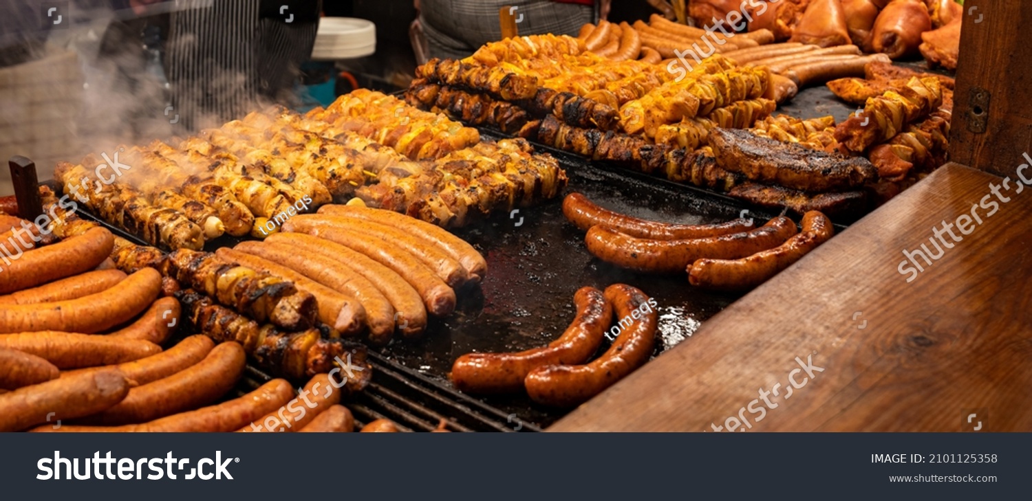 Lots of tasty juicy meat, bbq, outdoors grill, sausages, shahlik, steam over hot grilled food, high resolution, wide shot, panoramic, warm colors. Traditional street food market stall closeup, nobody #2101125358