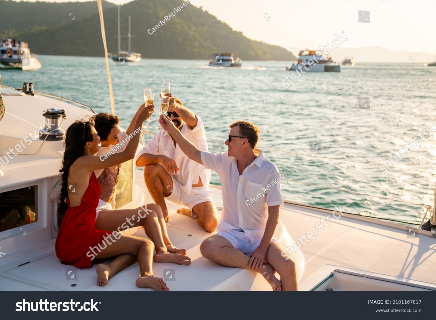 Group of man and woman friends enjoy party drinking champagne with talking together while catamaran boat sailing at summer sunset. Male and female relax outdoor lifestyle on tropical travel vacation #2101167817