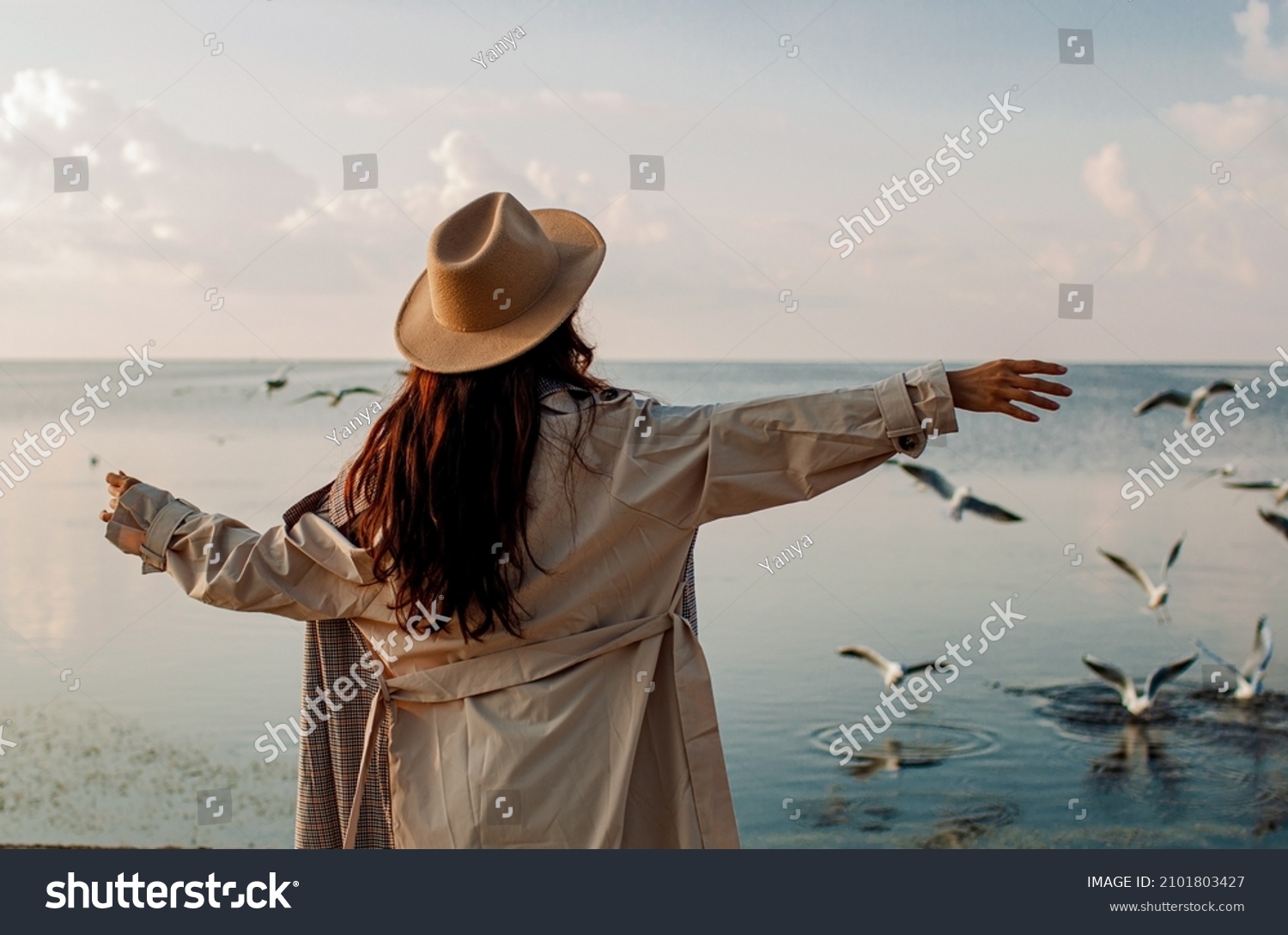 Young woman feeds seagulls at winter sea beach. Amazing coastline scene with girl. Concept of freedom, travel, flying. Lifestyle moment. #2101803427