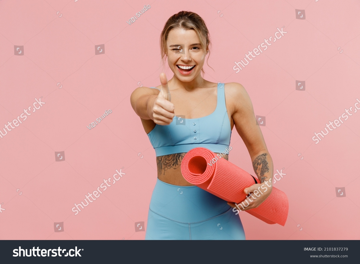 Young strong sporty athletic fitness trainer instructor woman wear blue tracksuit spend time in home gym show thumb up gesture blink isolated on pastel plain pink background. Workout sport concept. #2101837279
