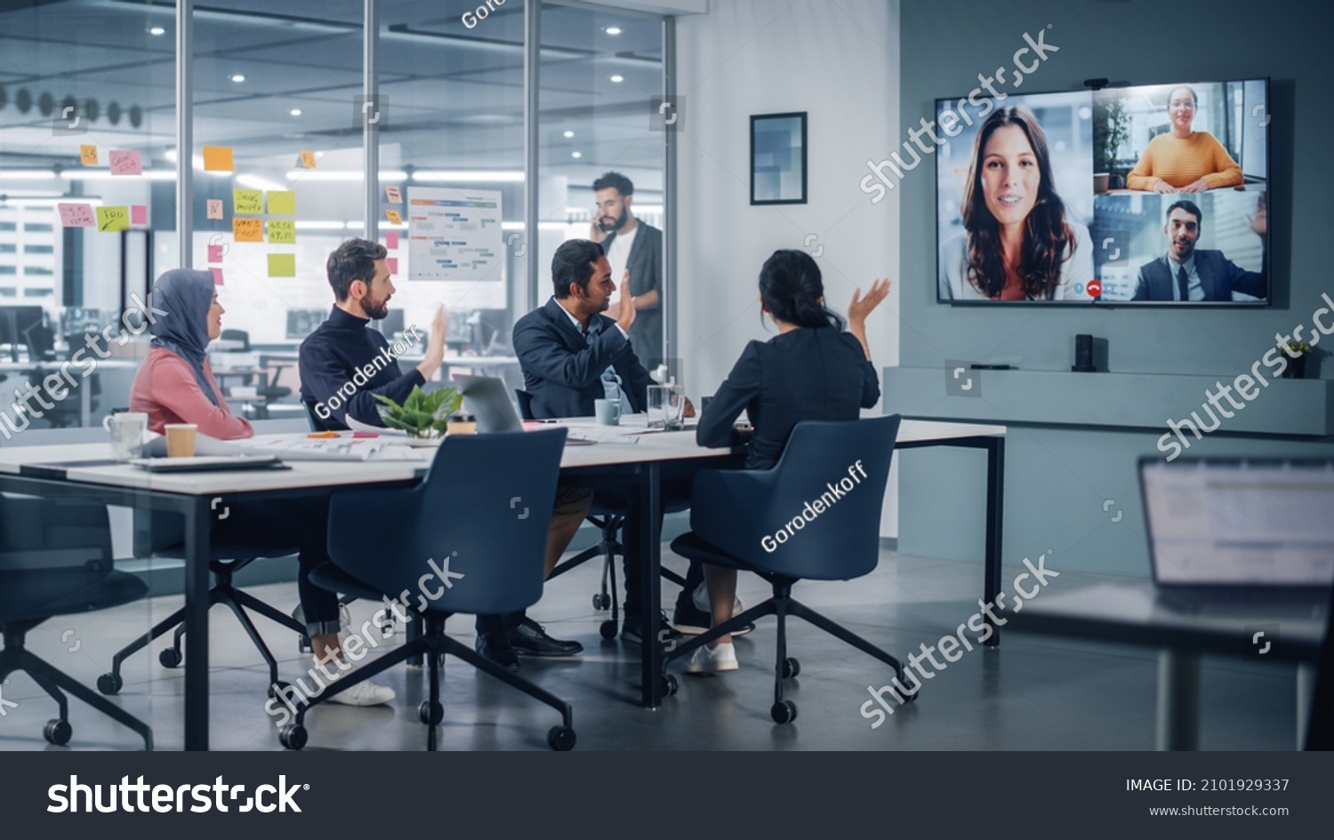 Businesspeople do Video Conference Call with Big Wall TV in Office Meeting Room. Diverse Team of Creative Entrepreneurs at Big Table have Discussion. Specialists work in Digital e-Commerce Startup #2101929337