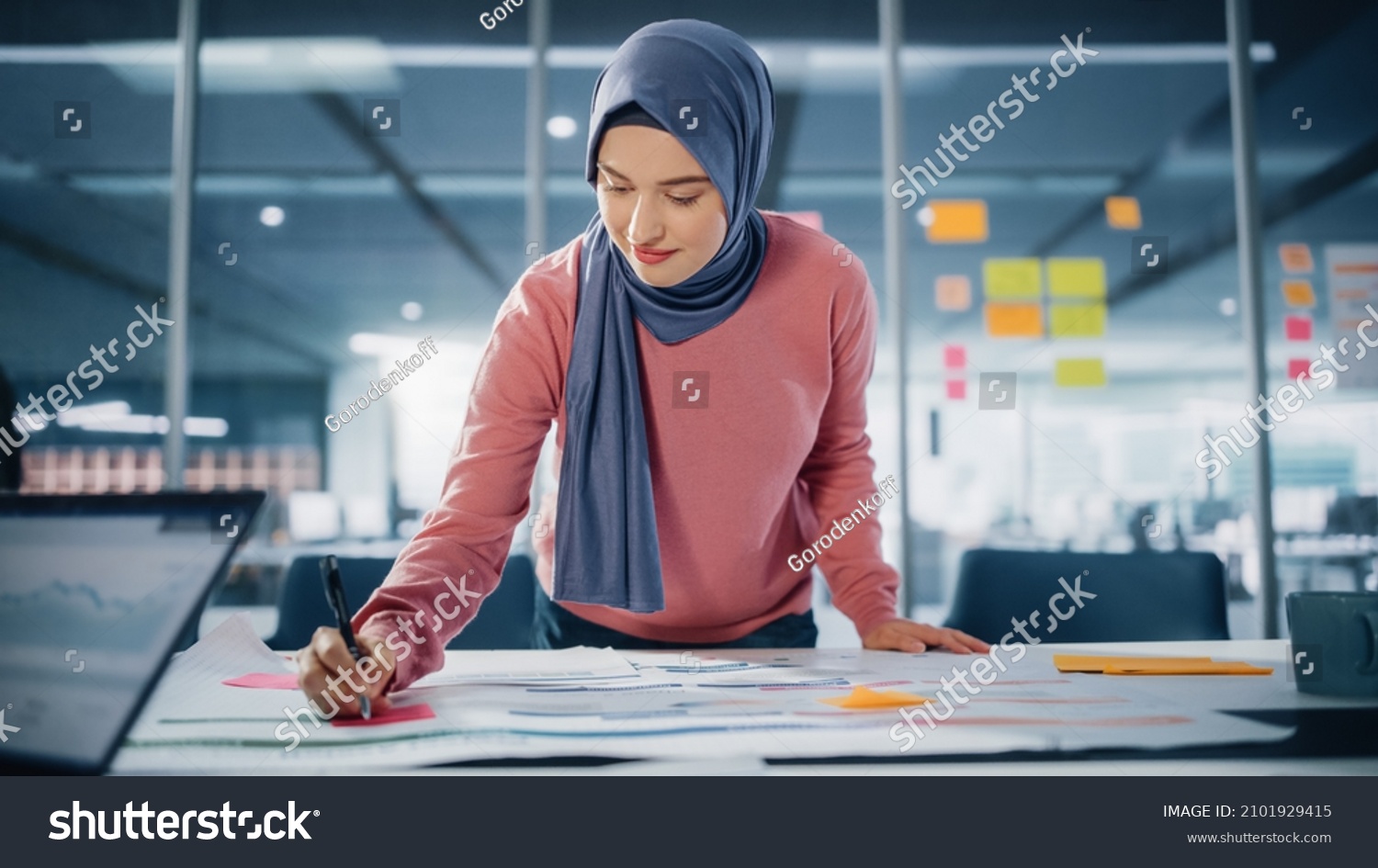 Modern Office: Motivated Muslim Businesswoman Wearing Hijab Works on Engineering Project, Does Document and Blueprints Analysis. Empowered Digital Entrepreneur Works on e-Commerce Startup Project #2101929415