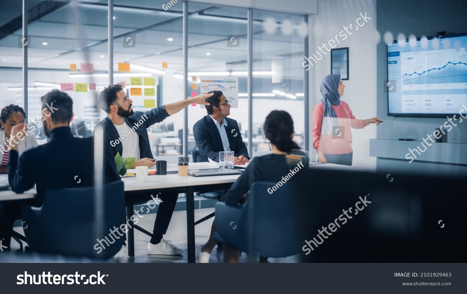 Multi-Ethnic Office Conference Room. Muslim Female CEO Wearing Hijab does Presentation for Group of Managers Talk, Use TV Infographics, Statistics. Businesspeople Brainstorm eCommerce Growth Strategy #2101929463