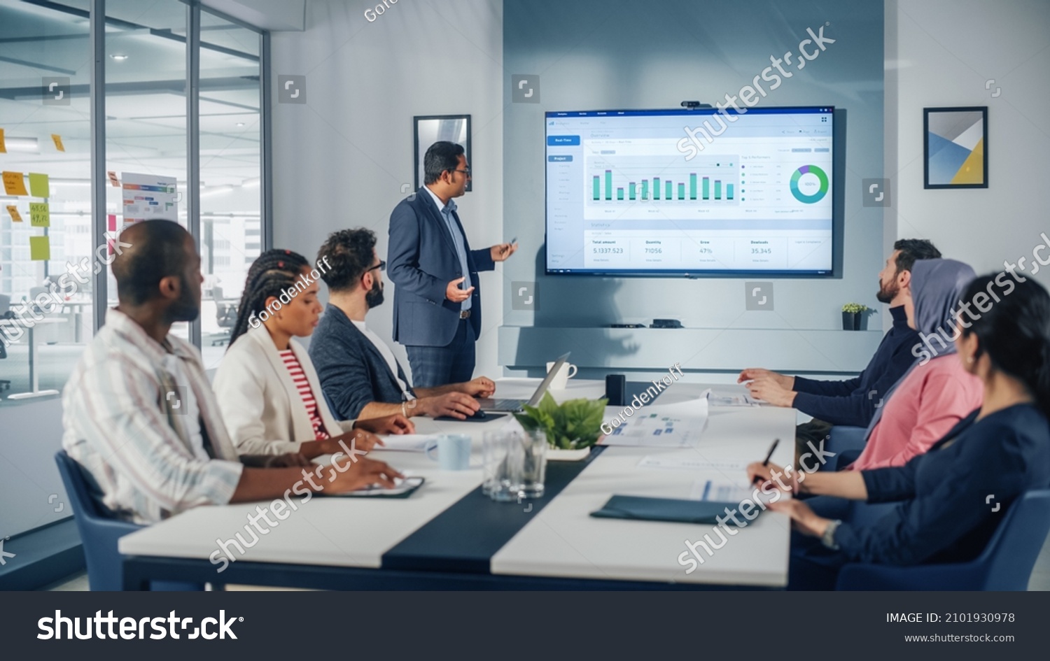 Multi-Ethnic Office Conference Room. Brilliant Indian Male CEO does Presentation for Multi-Ethnic Group of Managers Talking, Using TV Infographics, Statistics, Graphs. Innovative Businesspeople #2101930978