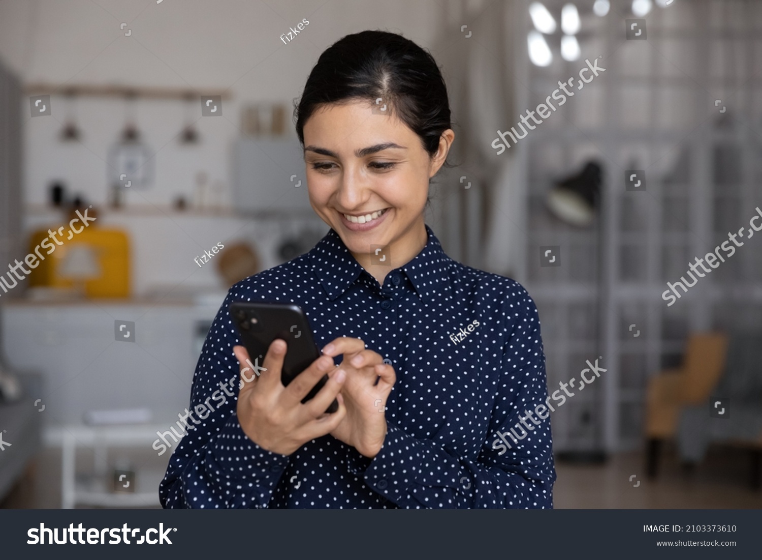 Happy millennial Indian girl, young woman reading text message on smartphone screen, smiling, feeling joy, chatting, typing, using online service, virtual app for payment on internet at home #2103373610