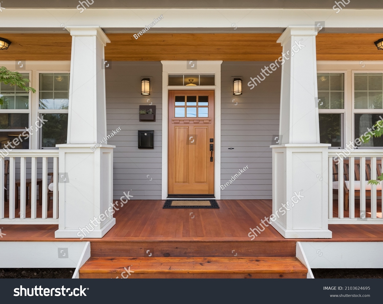 Front door and covered porch of new home exterior: solid wood door is flanked by sconce lights and has glass panels in upper portion and mullions. #2103624695