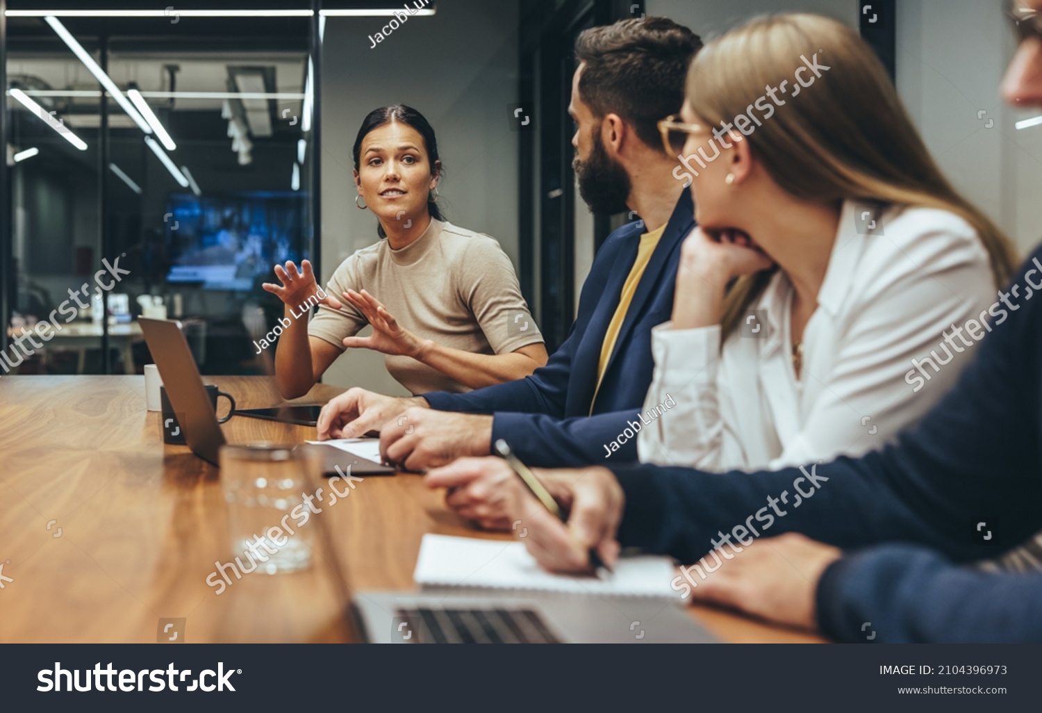 Young businesswoman leading a discussion during a meeting with her colleagues. Group of diverse businesspeople working together in a modern workplace. Business colleagues collaborating on a project. #2104396973