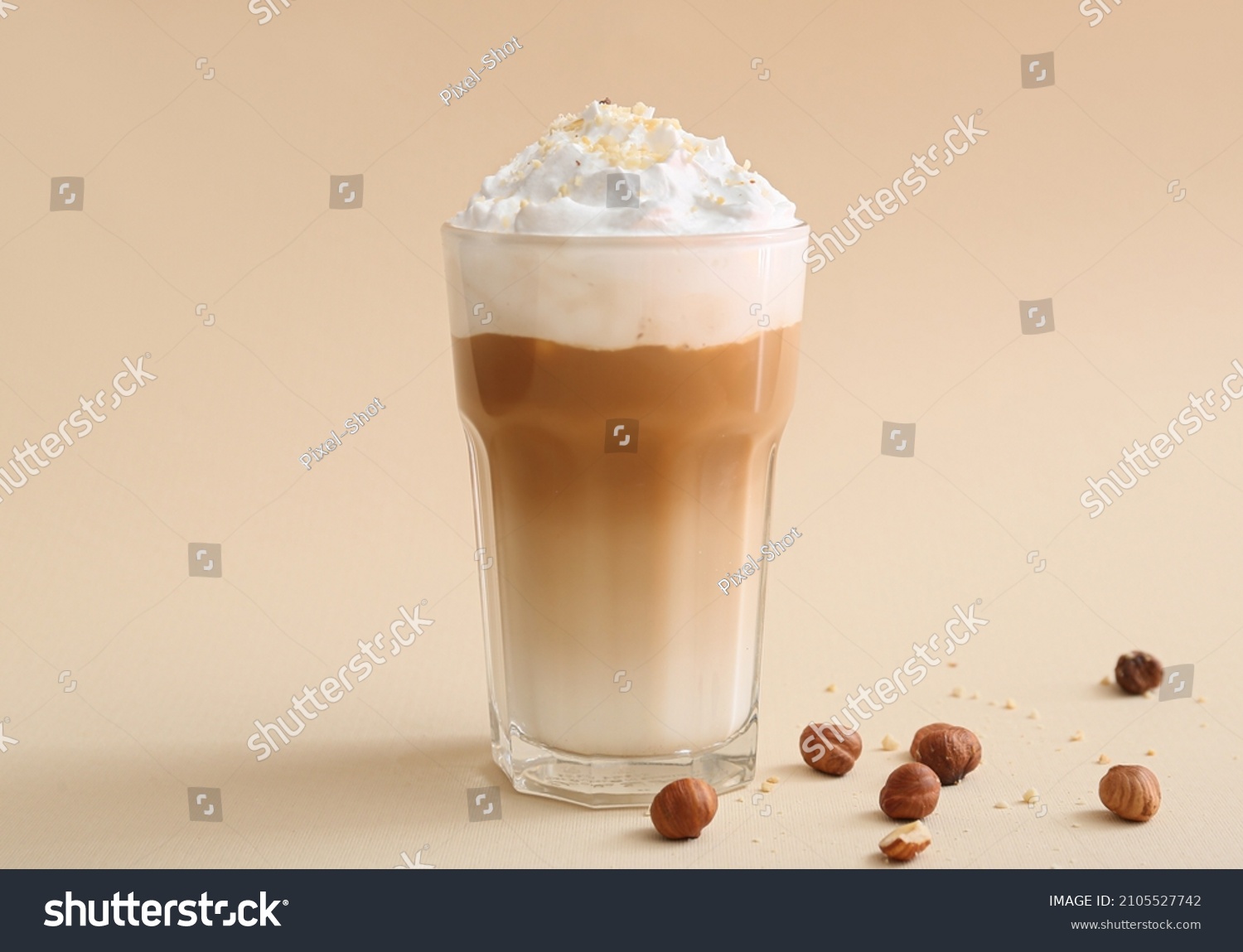 Glass of tasty latte with nuts on beige background #2105527742