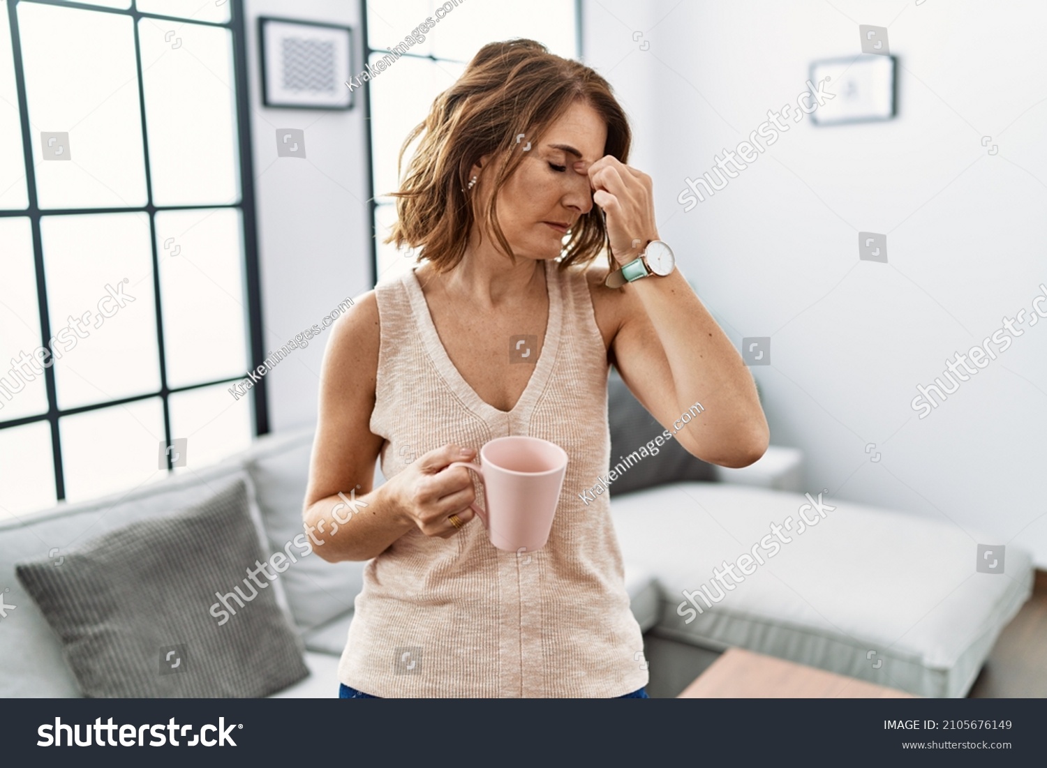 Middle age woman drinking a cup coffee at home tired rubbing nose and eyes feeling fatigue and headache. stress and frustration concept.  #2105676149