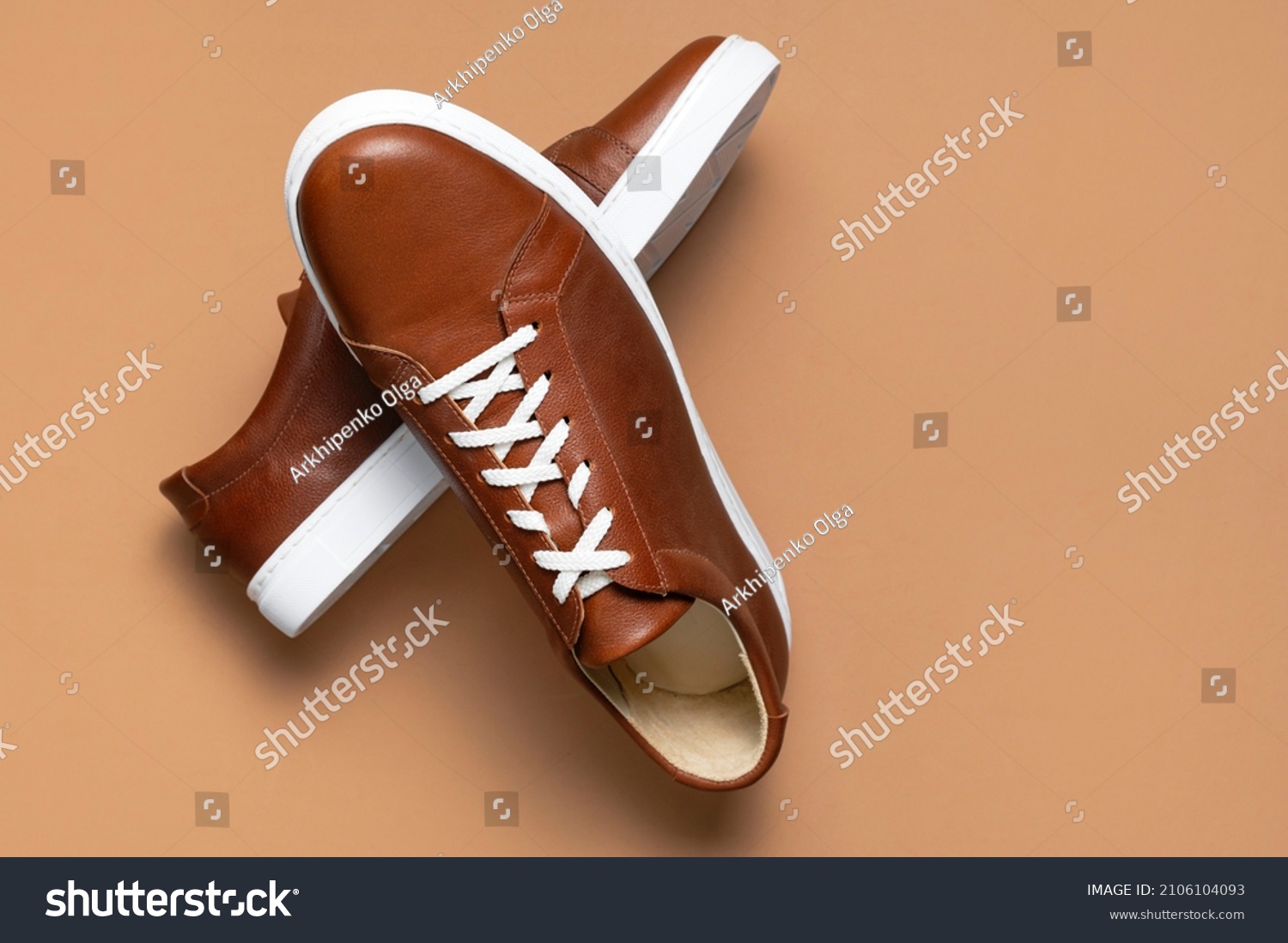 Leather brown men's sneakers with white laces and rubber soles on beige background. Flat lay top view. Men's sports casual shoes. Fashionable sneakers. Male fashion hipster footwear Minimal background #2106104093