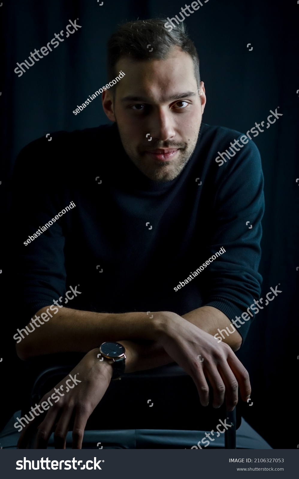 portrait of a young man sitting on a stool with his arms crossed and a seductive look #2106327053