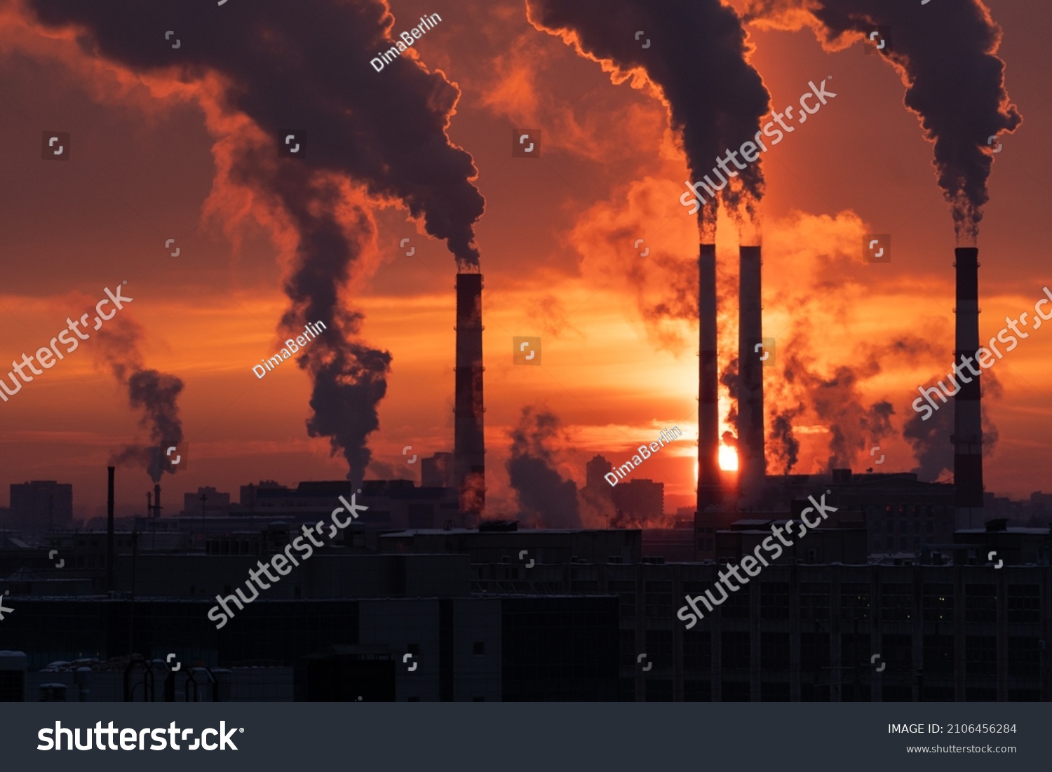 Smoke from heating station in big city during winter season at sunset. Smokestack pipes emitting co2 from coal thermal power plant into atmosphere. Air pollution and emission ecology problem concept #2106456284