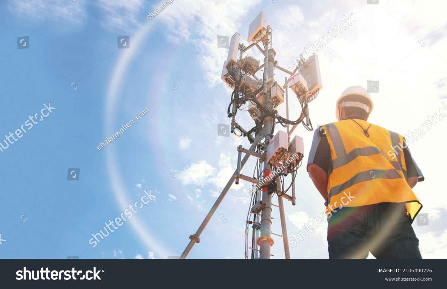 Helmeted asian male engineer works in the field with a telecommunication tower that controls cellular electrical installations to inspect and maintain 5G networks installed on high-rise buildings. #2106490226