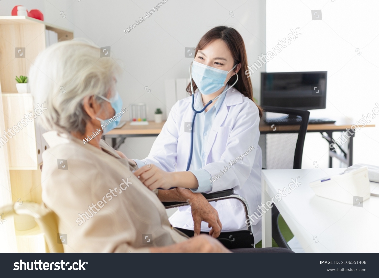 Asian doctor talk with old female patient about disease symptom, doctor use stethoscope listening lung of patient, elderly health check up , they wear surgical mask on white background, corona virus  #2106551408