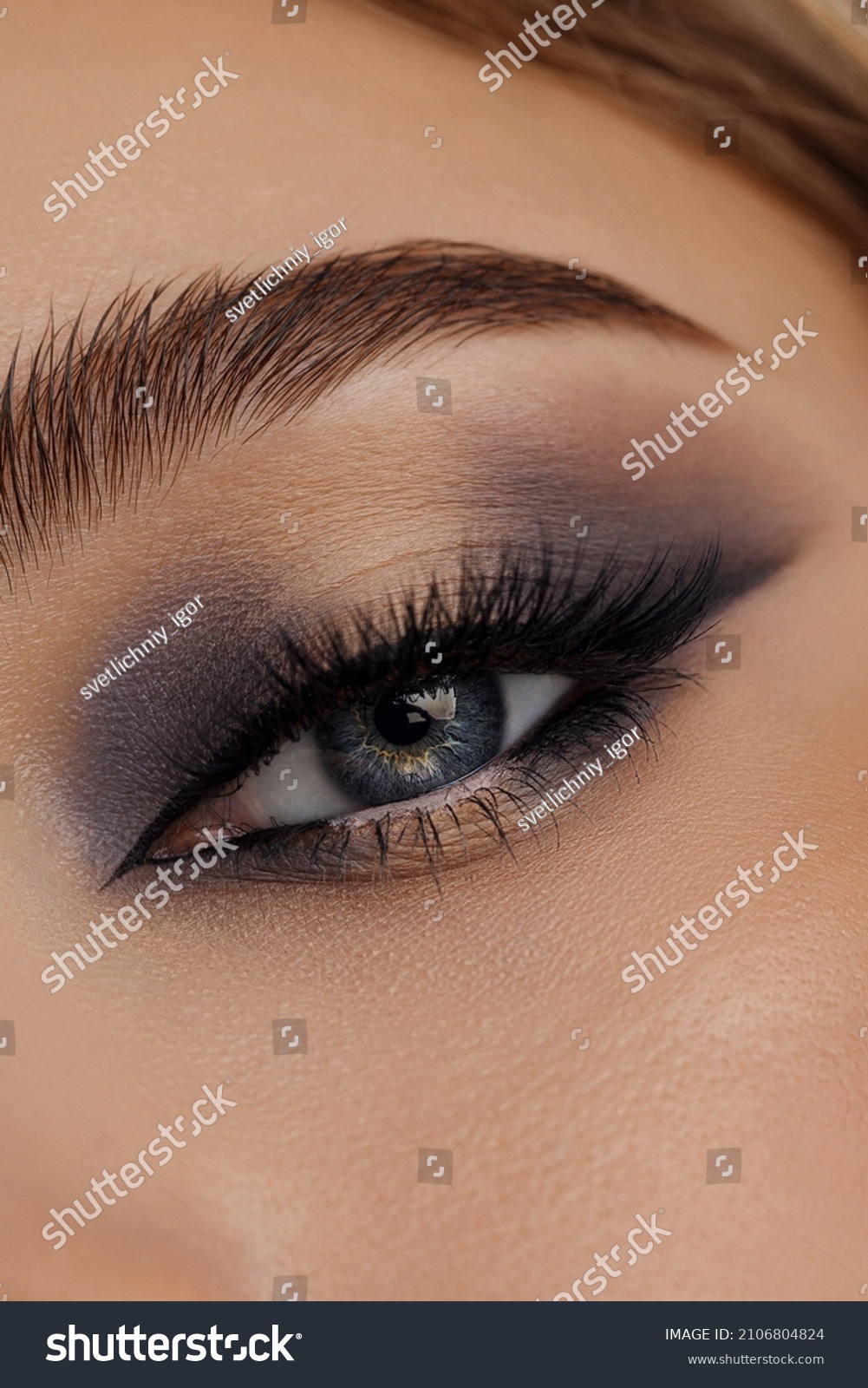 Beautiful macro shot of female eye make-up in smoky eyes style. Blue eye. Creative make-up. Perfect shape make-up and long lashes. Cosmetics. Beautiful eyes make-up. Close-up #2106804824