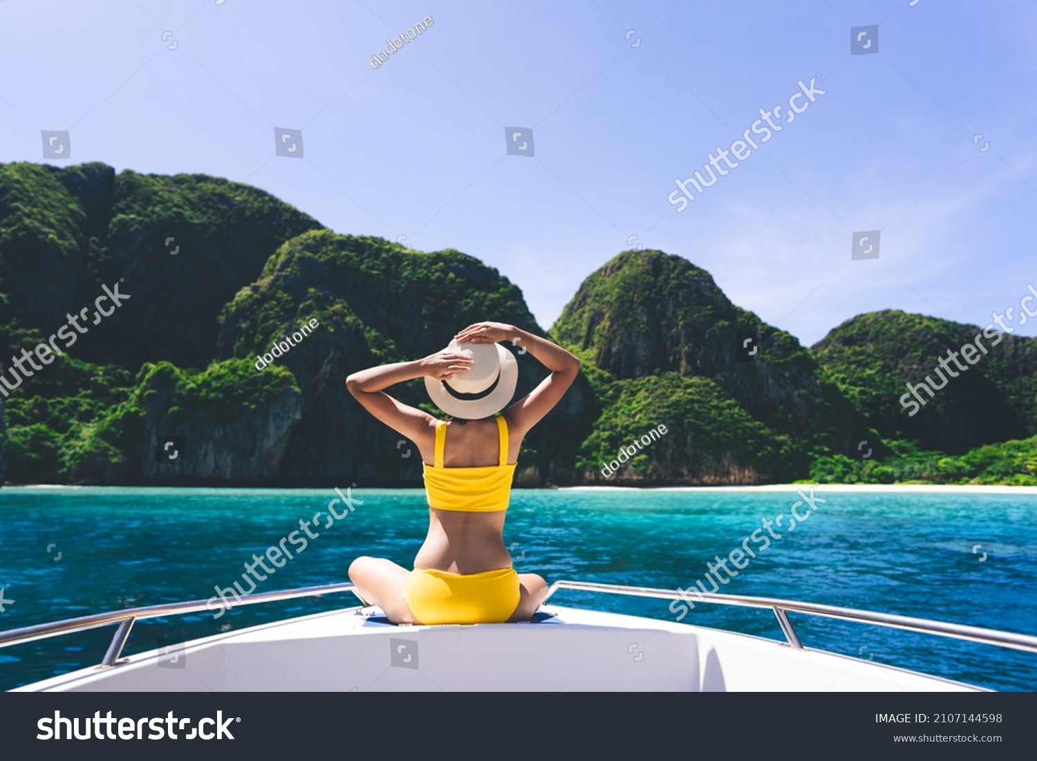 Rear view of adult traveling woman sit and relax on the sailing boat wear yellow bikini blue sky and sea. Summer vacation island domestic trip at Maya bay. Krabi, Thailand #2107144598