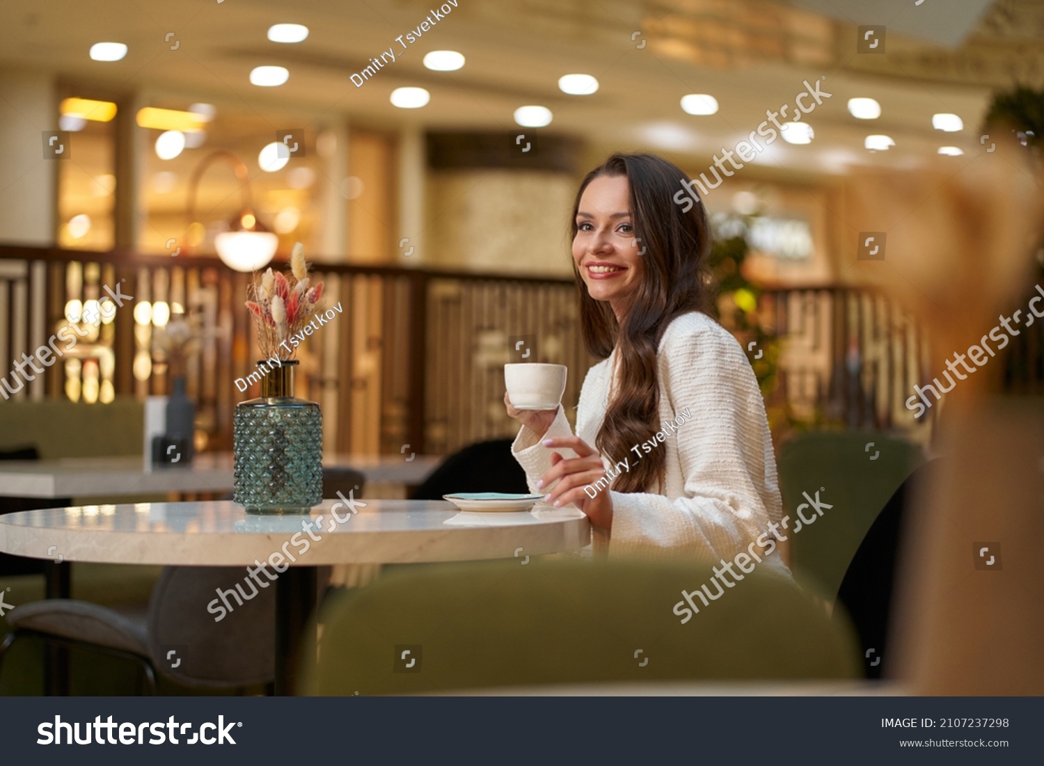 Young beautiful stylish woman in white blazer with cup od coffee sitting in restaurant #2107237298