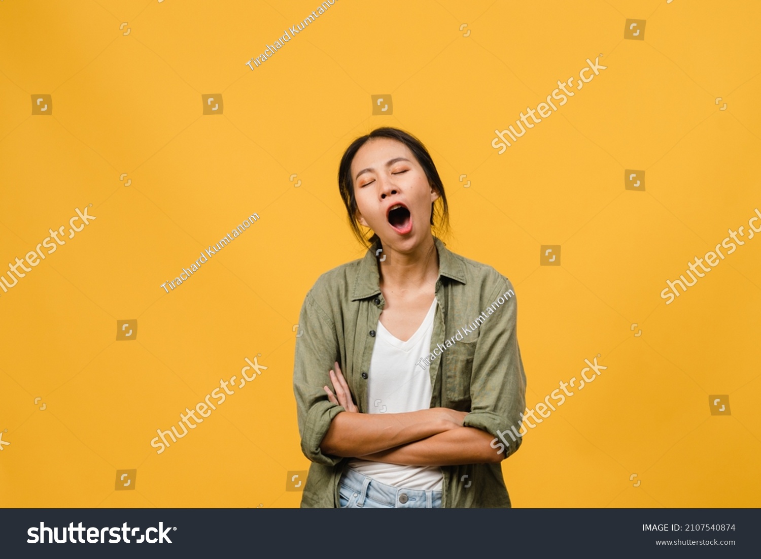 Portrait of Young Asia lady with negative expression, bored yawning tired covering mouth with hand in casual clothing isolated on yellow background with blank copy space. Facial expression concept #2107540874