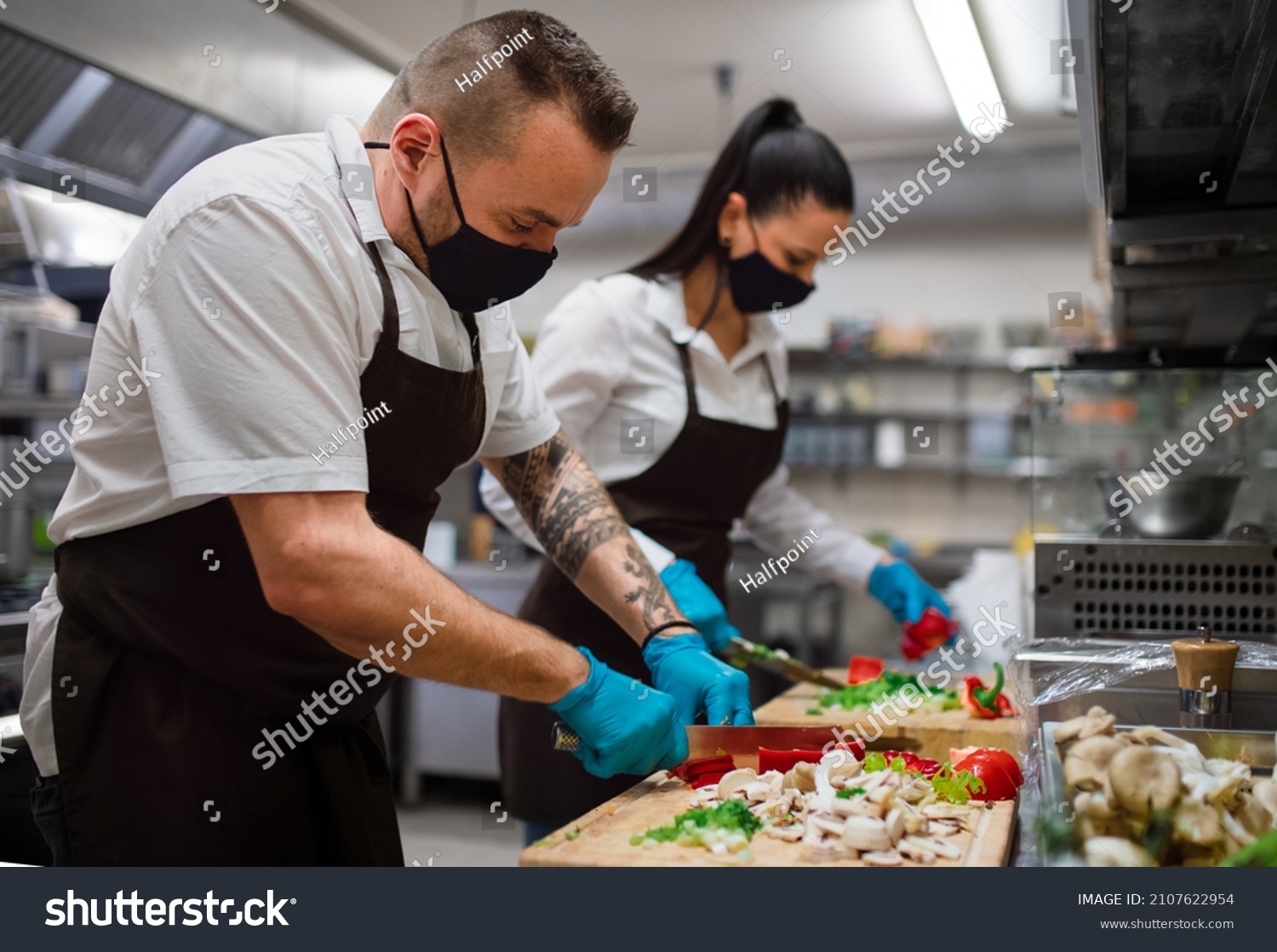Chef and cook with face masks cutting vegetables indoors in restaurant kitchen, coronavirus concept. #2107622954