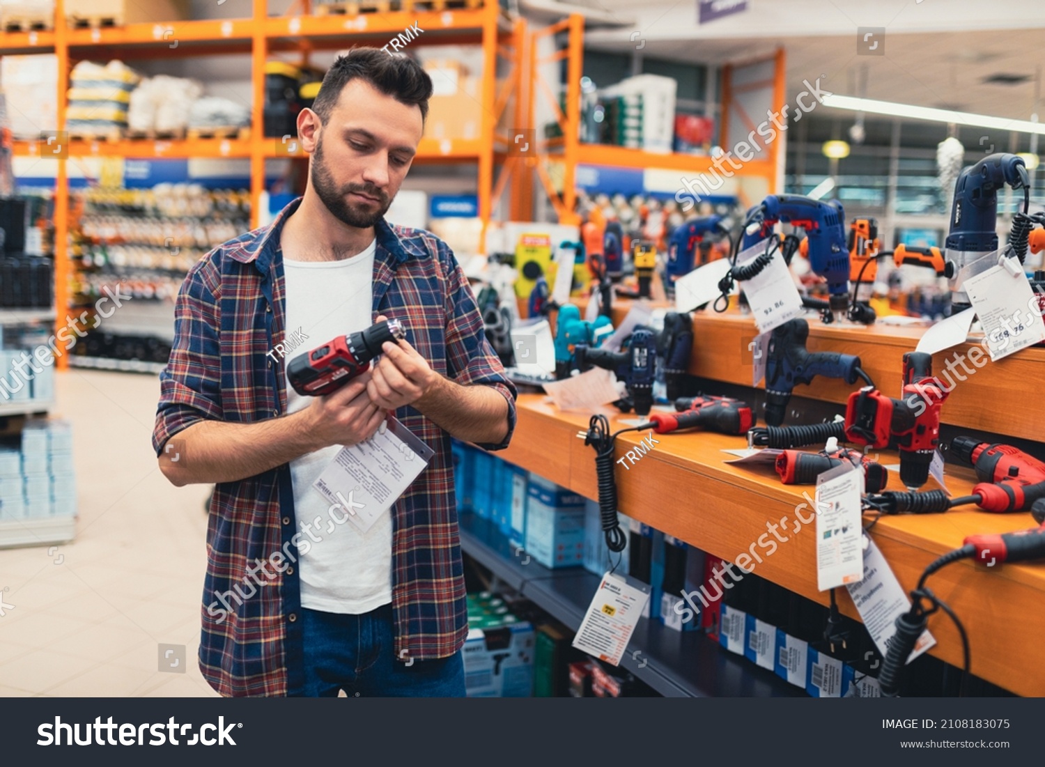 a man in a hardware store chooses a new screwdriver next to a showcase of power tools for repairs in the house #2108183075