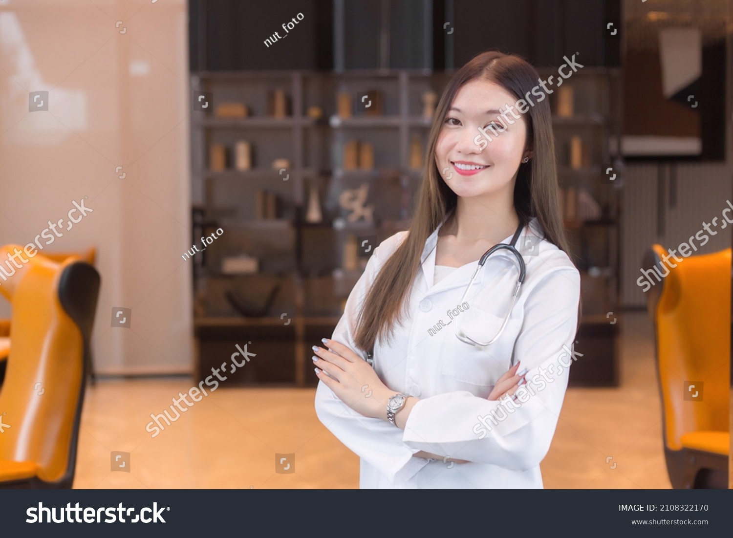 Asian woman doctor Standing smile in a good mood with arms crossed in the office room in the hospital. Wearing a white robe and stethoscope. #2108322170