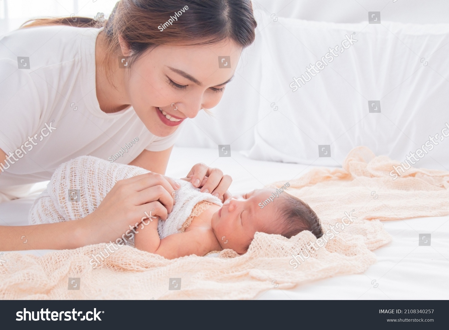 Selective focus of Asian young mother swaddling baby on bed, Beautiful woman wrapping adorable infant in thin cloth. Cute newborn child taking nap after bath. Concept of baby care and family. #2108340257