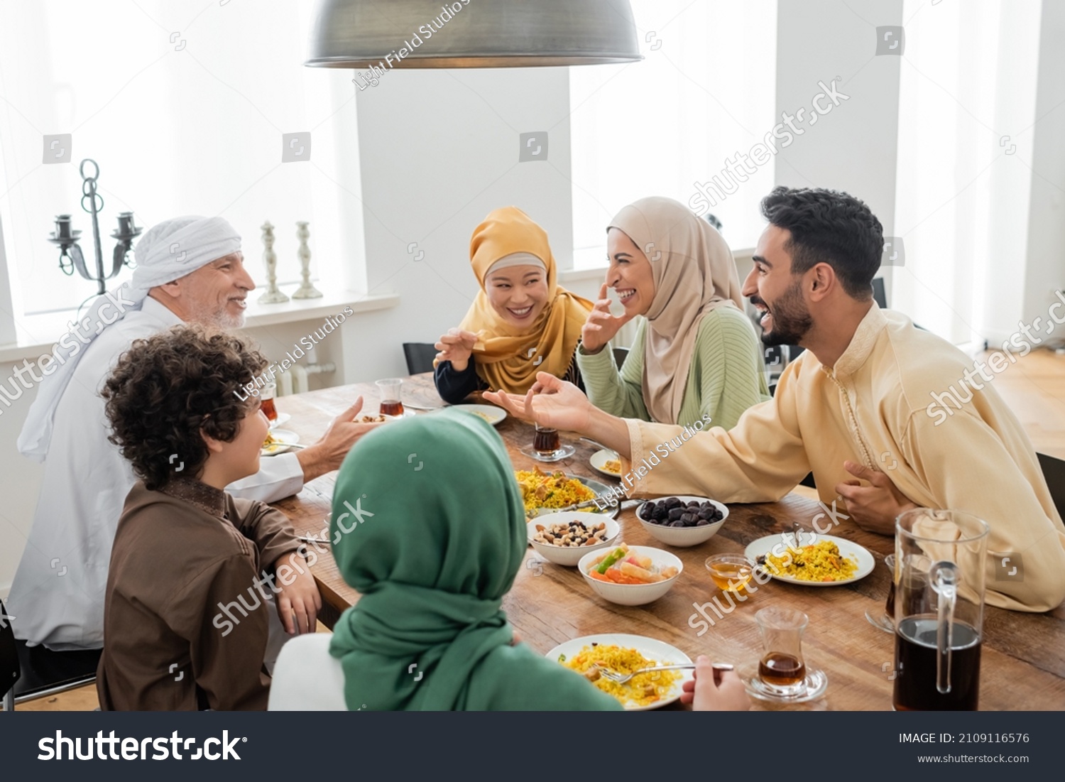 young arabian man talking to cheerful multicultural muslim family during dinner #2109116576