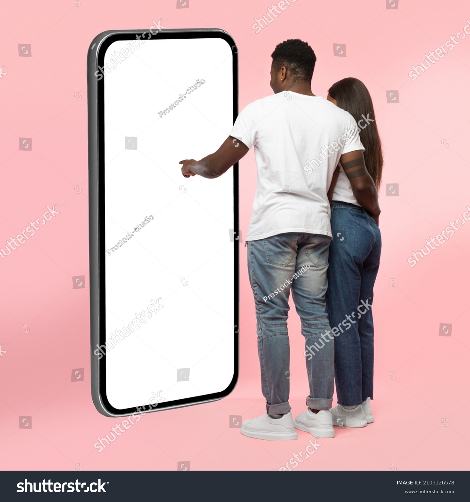 Rear Back View Of Black Couple Using Big Smartphone With Blank White Screen Touching Huge Display Panel With Finger, Guy Higging Lady Standing On Pink Background, Mock Up. Full Body Length #2109126578