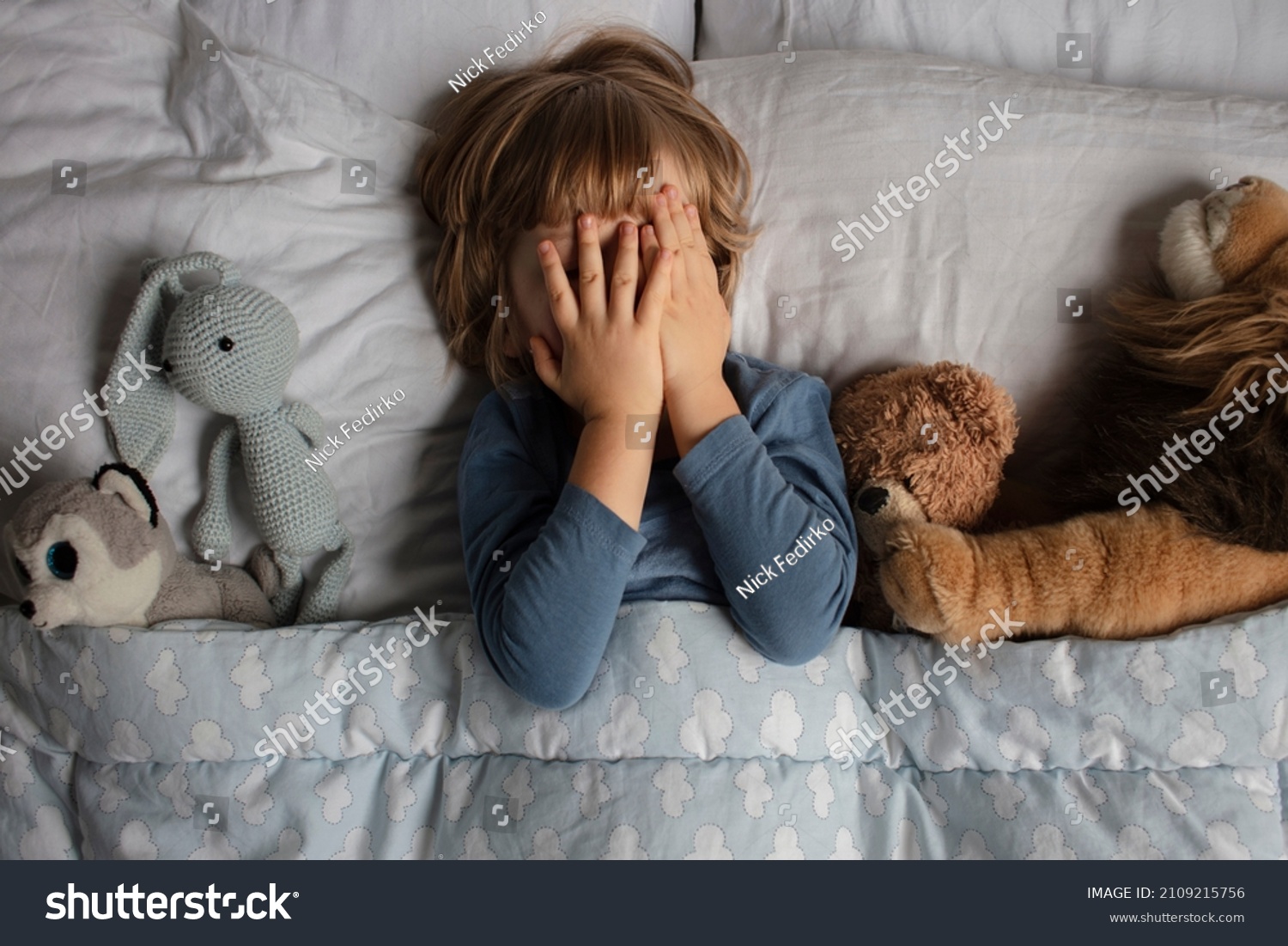 The child was scared before going to bed. Night terrors in a child. The kid covers his face with his hands in a fear. Children's experiences. Boy in the bed. View from above. Sad psychological state. #2109215756