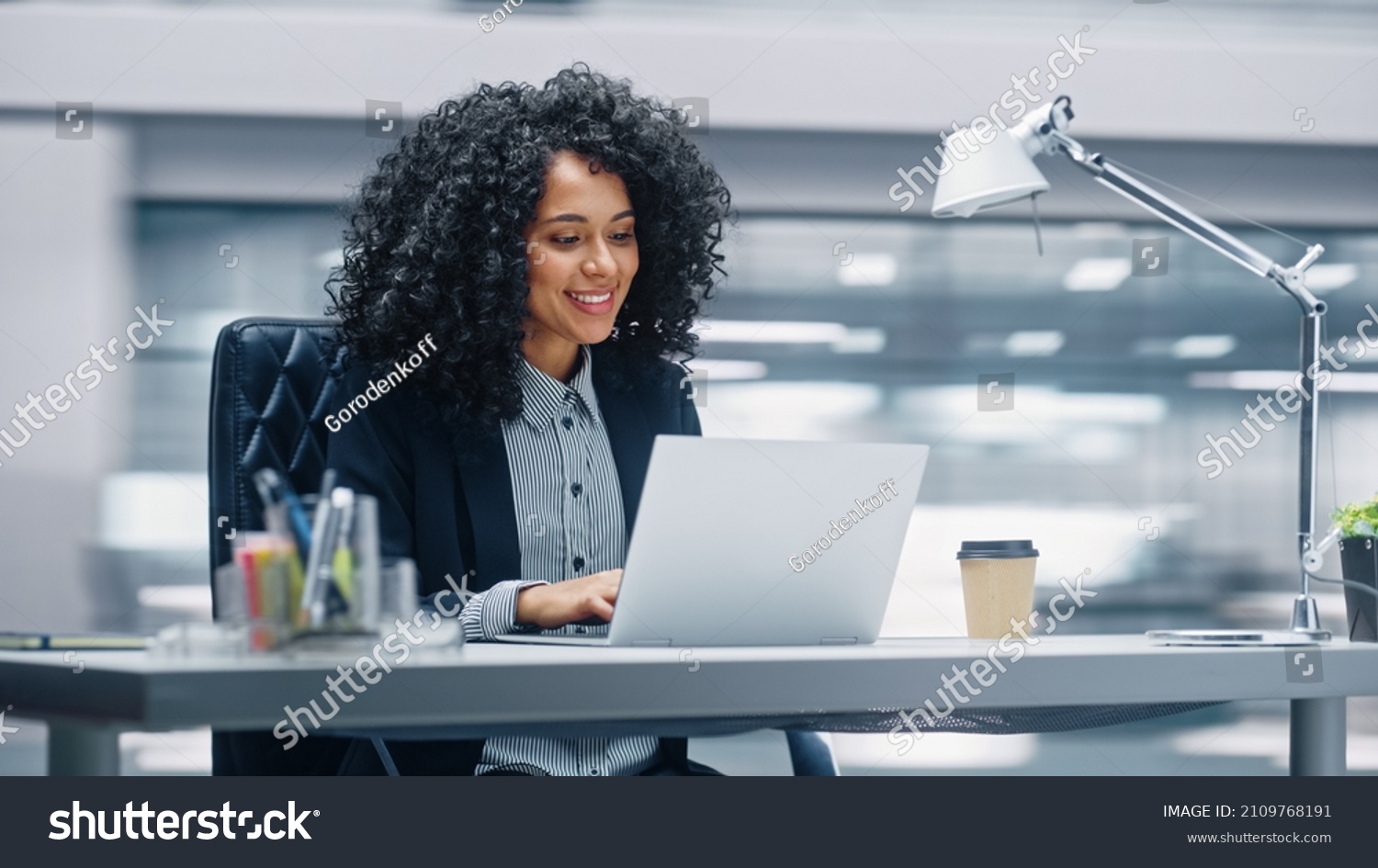 Modern Office: Black Businesswoman Sitting at Her Desk Working on a Laptop Computer. Smiling Successful African American Woman working with Big Data e-Commerce. Motion Blur Background #2109768191