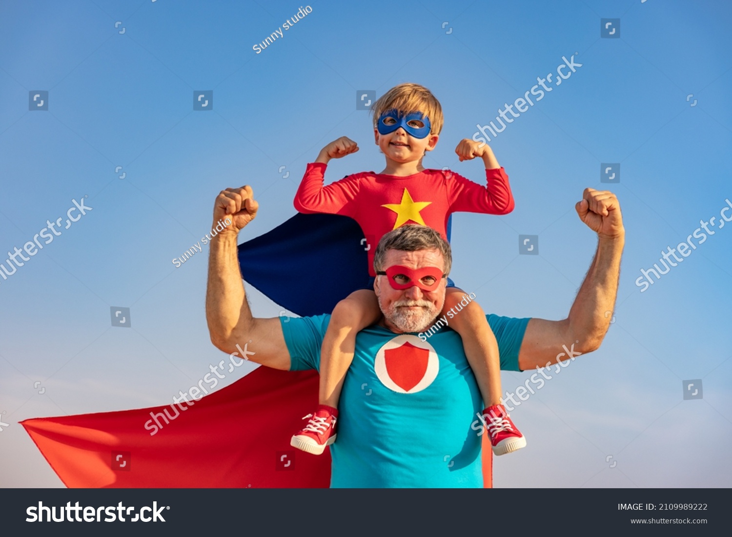 Superhero senior man and child playing outdoor. Super hero grandfather and boy having fun together against blue summer sky background. Family holiday concept. Happy Father's day #2109989222