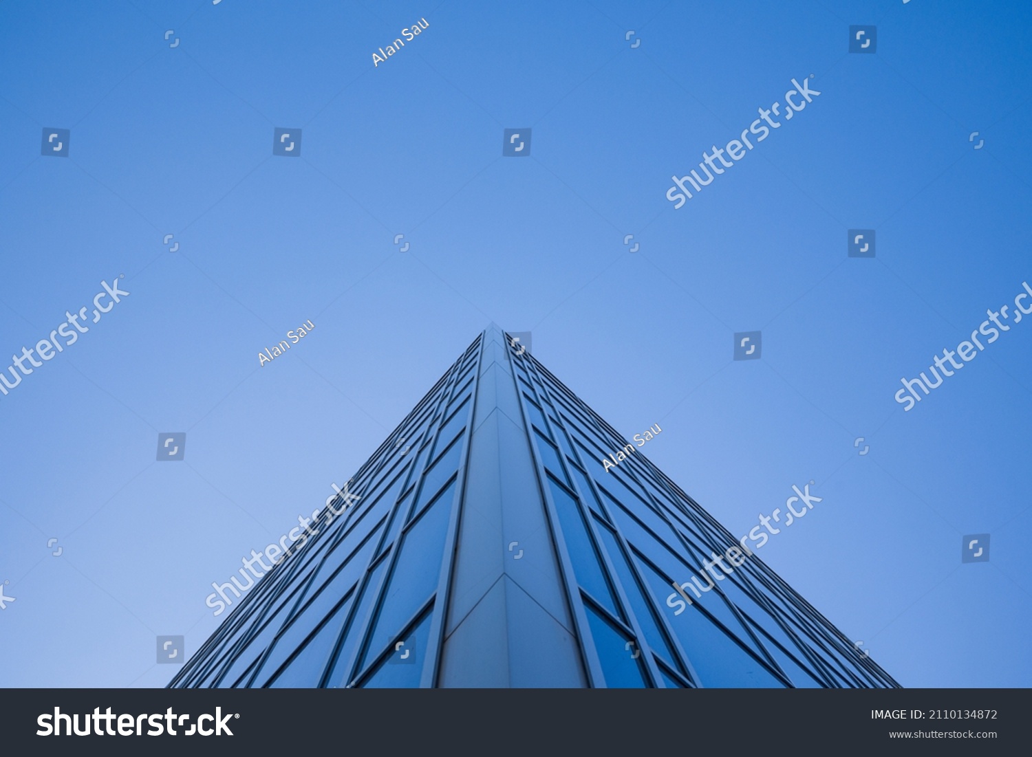 Low angle view of glass facade of tall office building against clear blue sky #2110134872