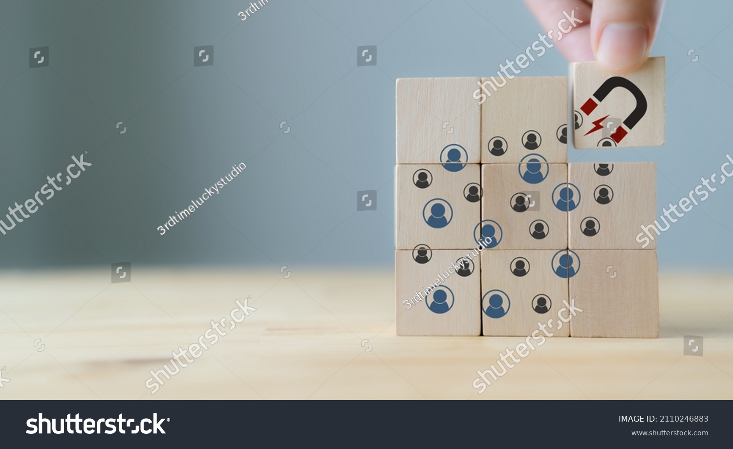 Attracting online customer and lead generation concept. Digital inbound marketing, customer retention strategy.Hand hold wooden cube with the icon big magnet to attract many people on grey background. #2110246883