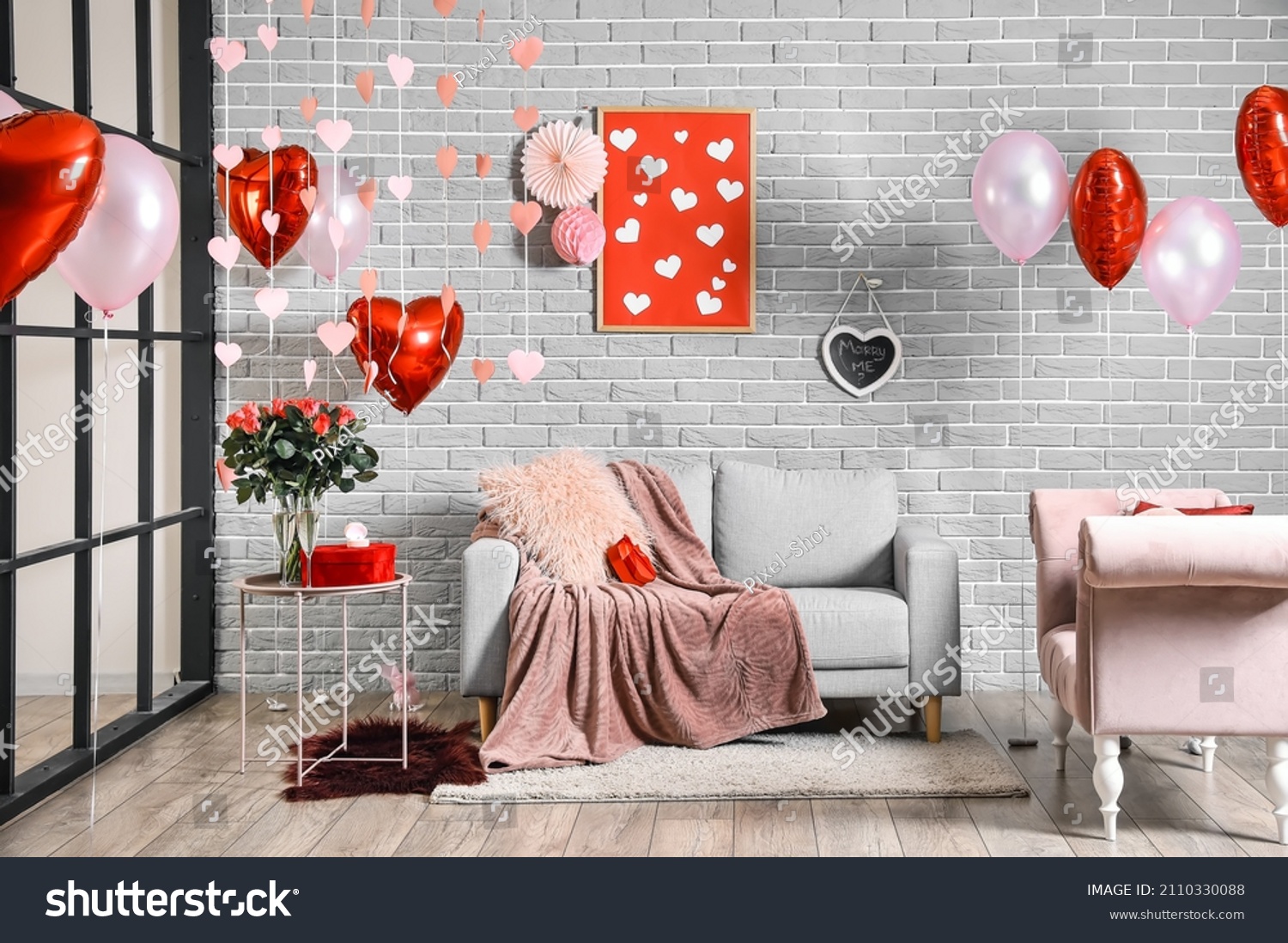 Interior of room decorated for Valentine's day with air balloons and comfortable sofas near grey brick wall #2110330088