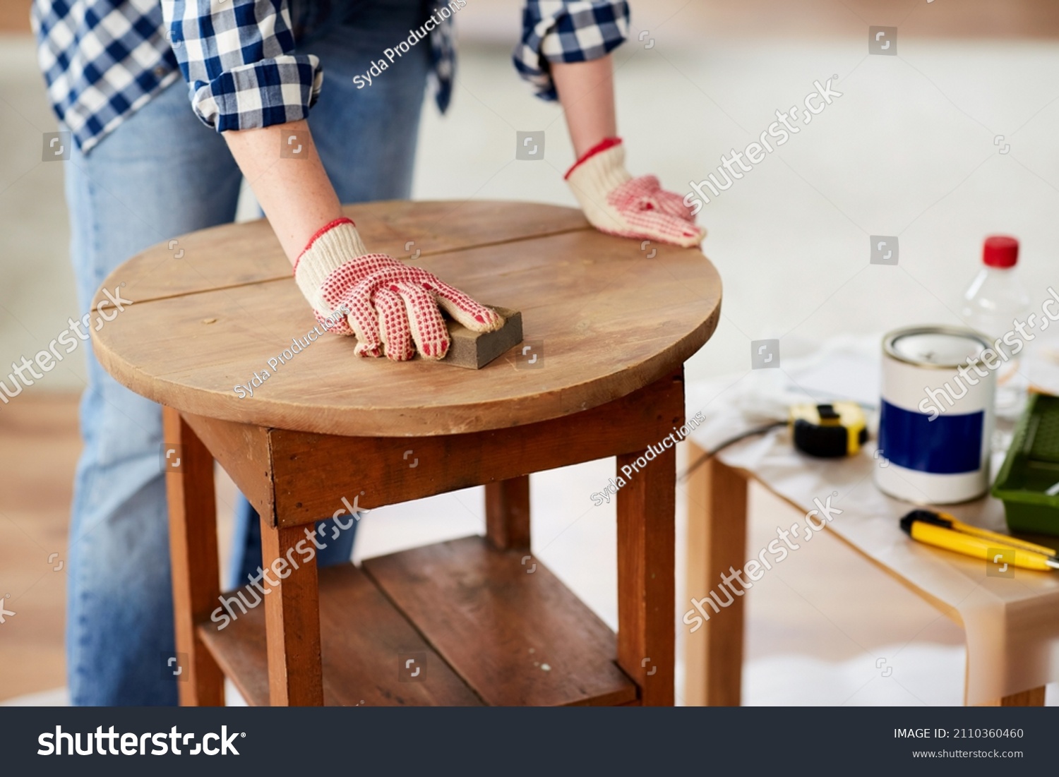 furniture renovation, diy and home improvement concept - close up of woman sanding old wooden table with sponge #2110360460