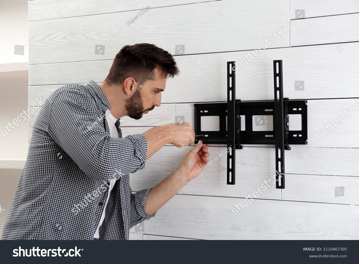 Man with screwdriver installing TV bracket on wall indoors #2110467305