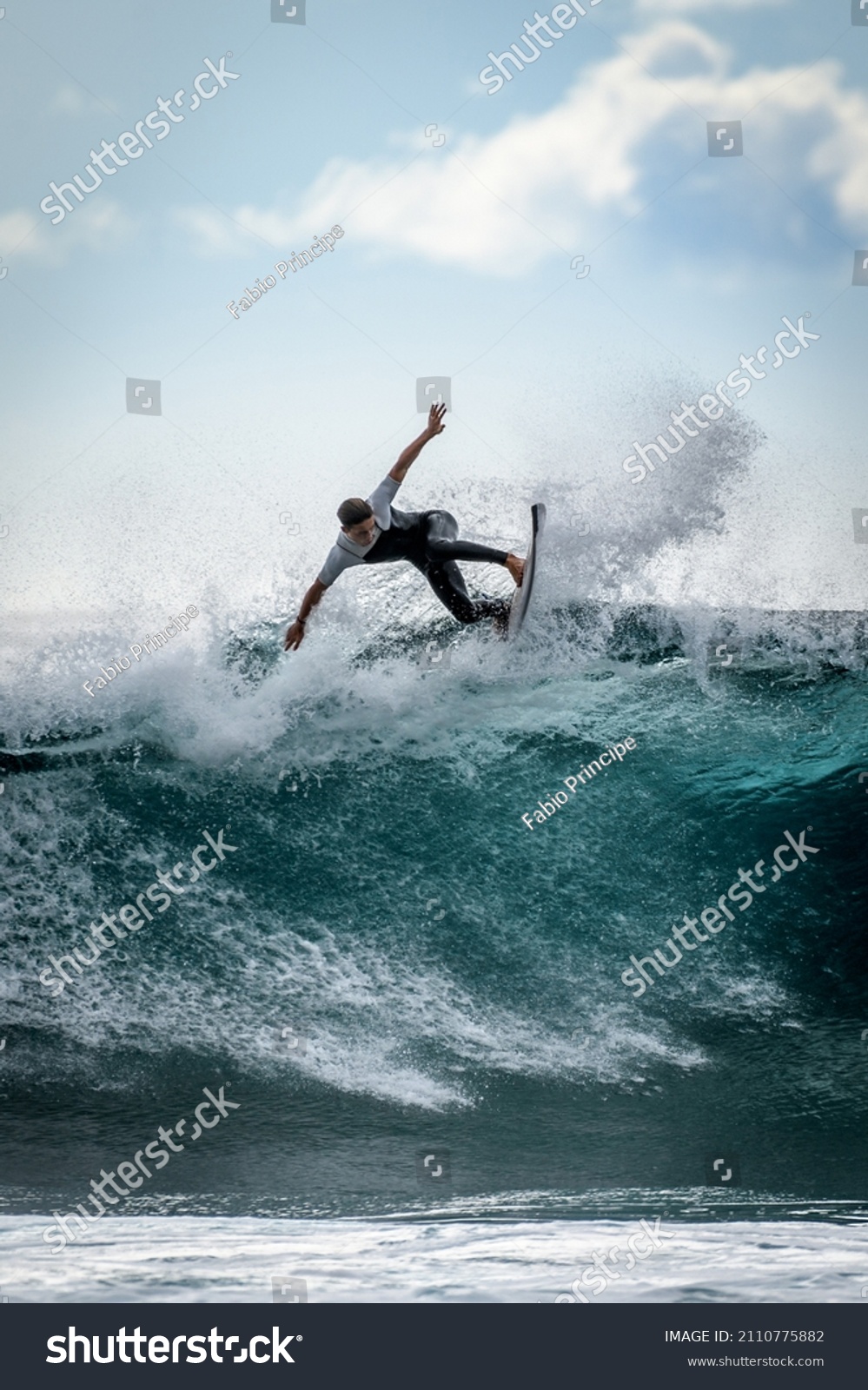 Young surfer with with wetsuit enjoying big waves in Tenerife, Canary Islands. Sporty boy riding his surf board on the ocean wave. Brave teenager making tricks on the rough sea during a competition. #2110775882