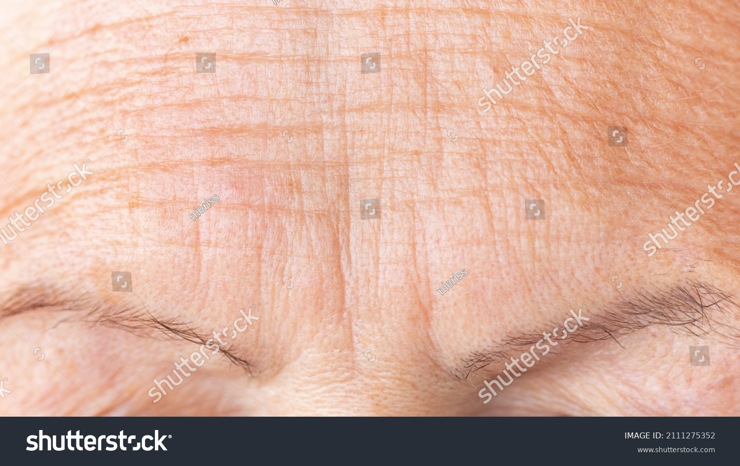 Wrinkled skin of a mature woman's forehead macro photography. Deep aging wrinkles close up. Prevention of age-related skin changes concept. Cosmetology procedures against aging and wrinkles concept. #2111275352