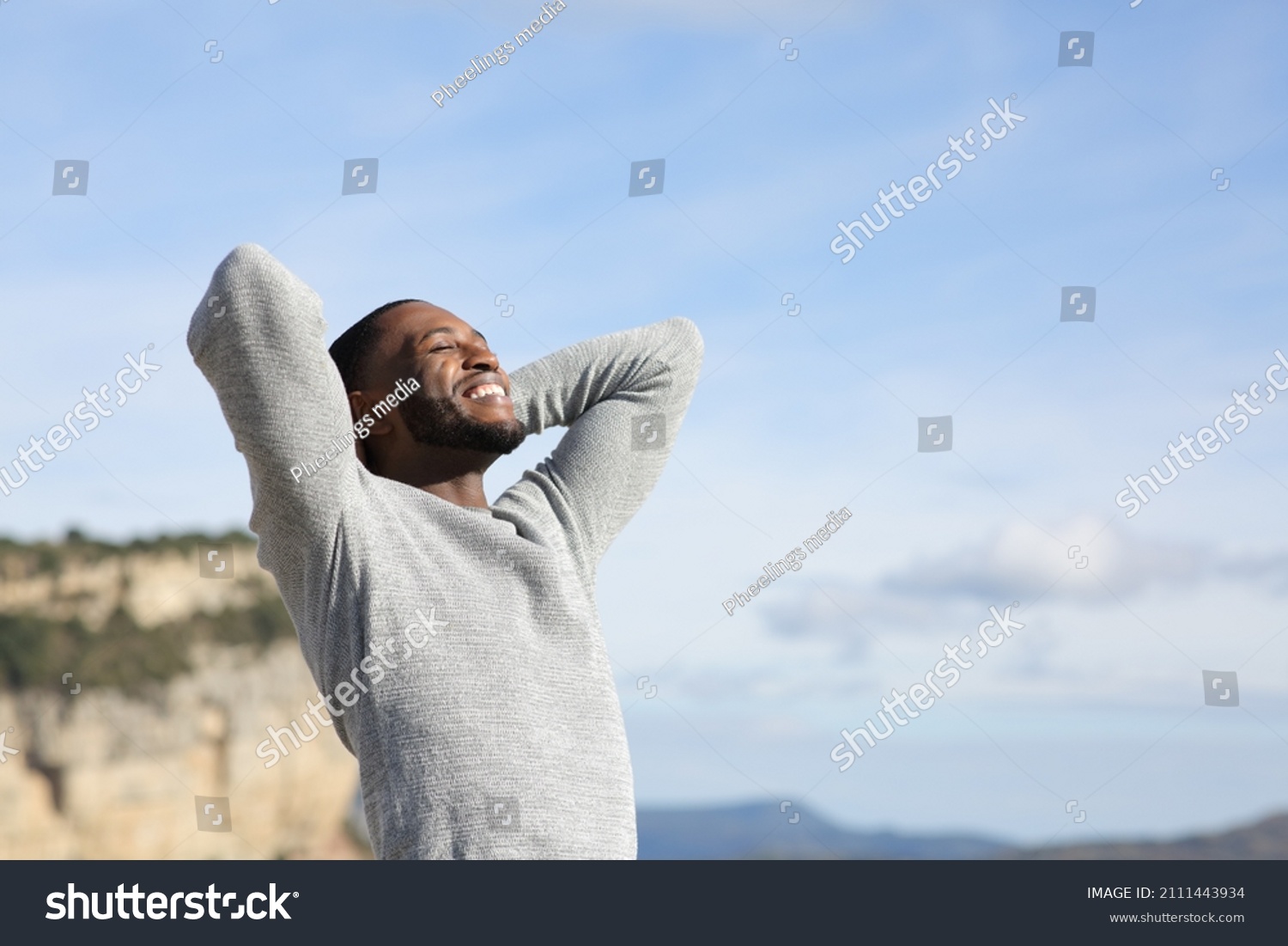 Relaxed man with black skin breathing fresh air with hands on head in the mountain #2111443934
