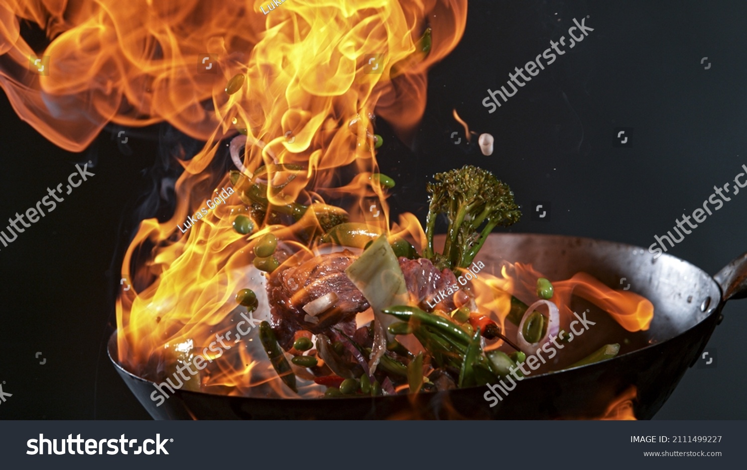 Freeze Motion of Wok Pan with Flying Ingredients in the Air and Fire Flames. #2111499227