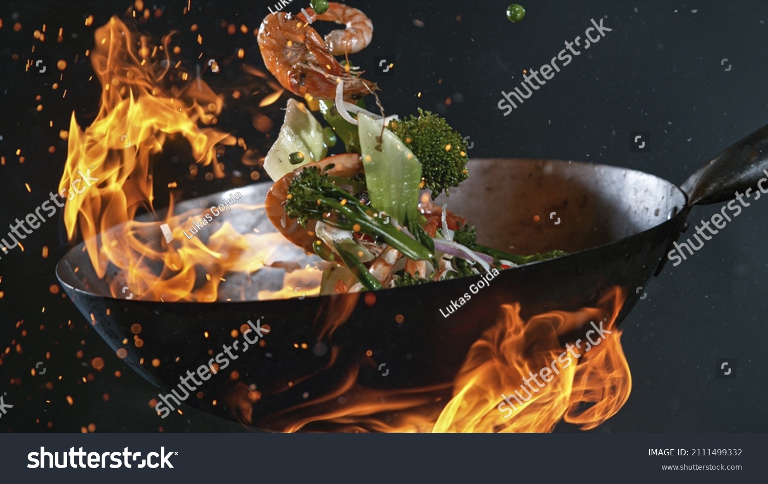 Freeze Motion of Wok Pan with Flying Ingredients in the Air and Fire Flames. #2111499332