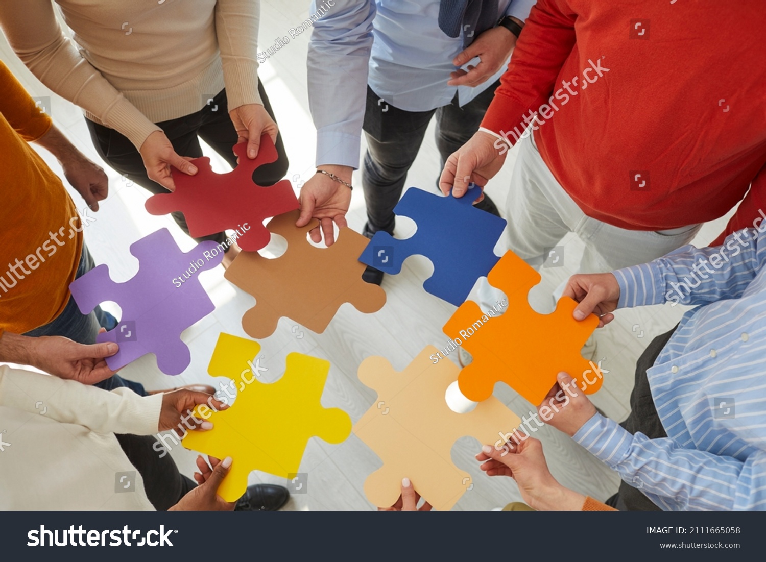 Close up top view of diverse multiracial businesspeople hold jigsaw pieces connect puzzle seek for business solution in office. Employees or colleagues involved in teambuilding activity or training. #2111665058